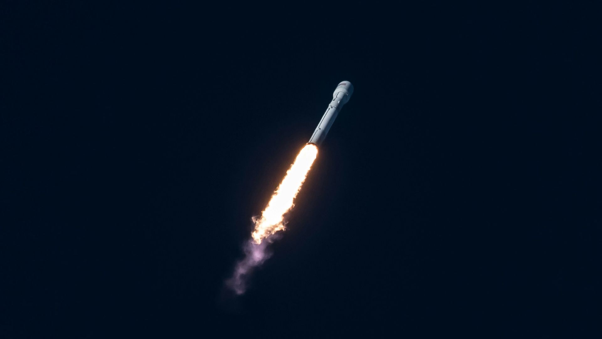 Spacecraft flying upward through bright sky with contrail behind