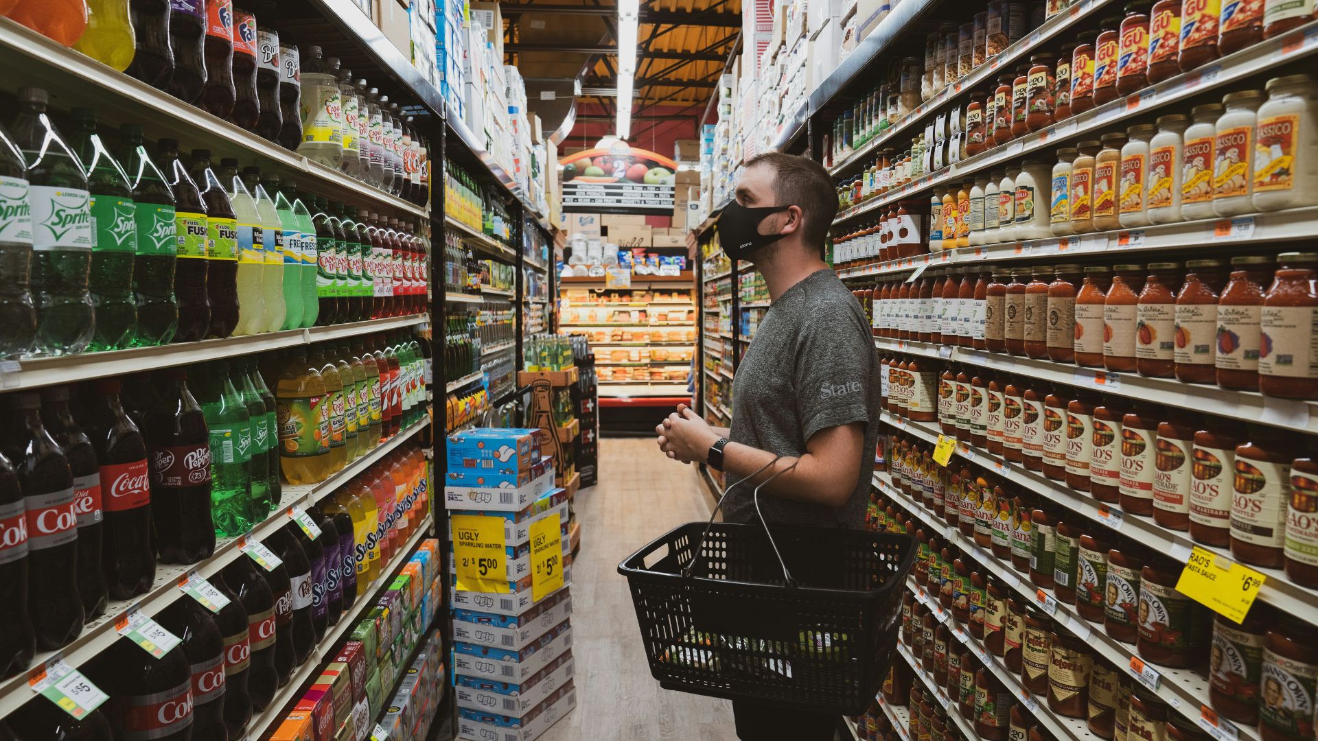 Man in a striped polo shirt holding a blue shopping basket in a grocery aisle.