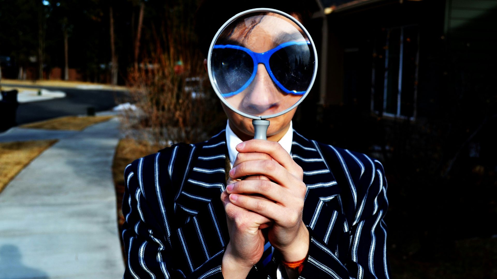 A person wearing sunglasses holding a magnifying glass