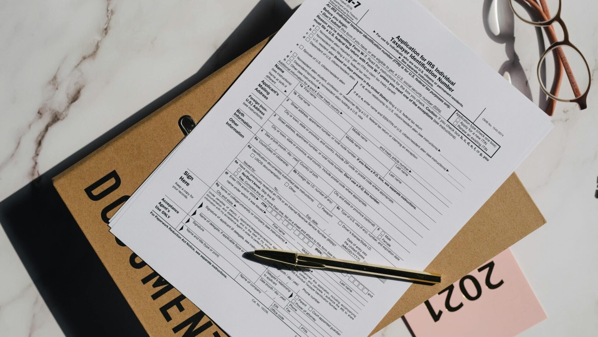 Ballpoint pen resting on a blank document next to eyeglasses on a wooden surface, ready for writing or signing.