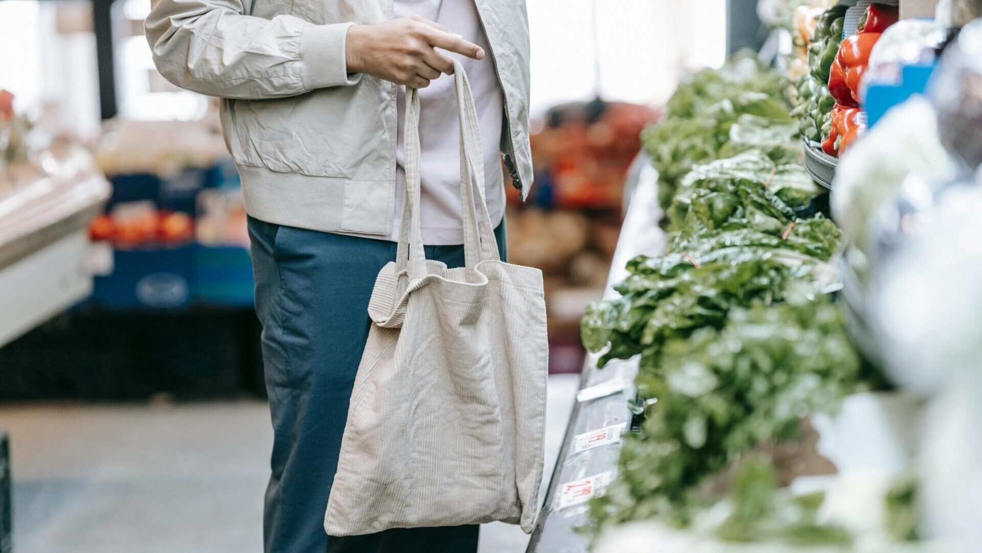 An unrecognizable customer selecting fresh vegetables in the produce section of a supermarket.