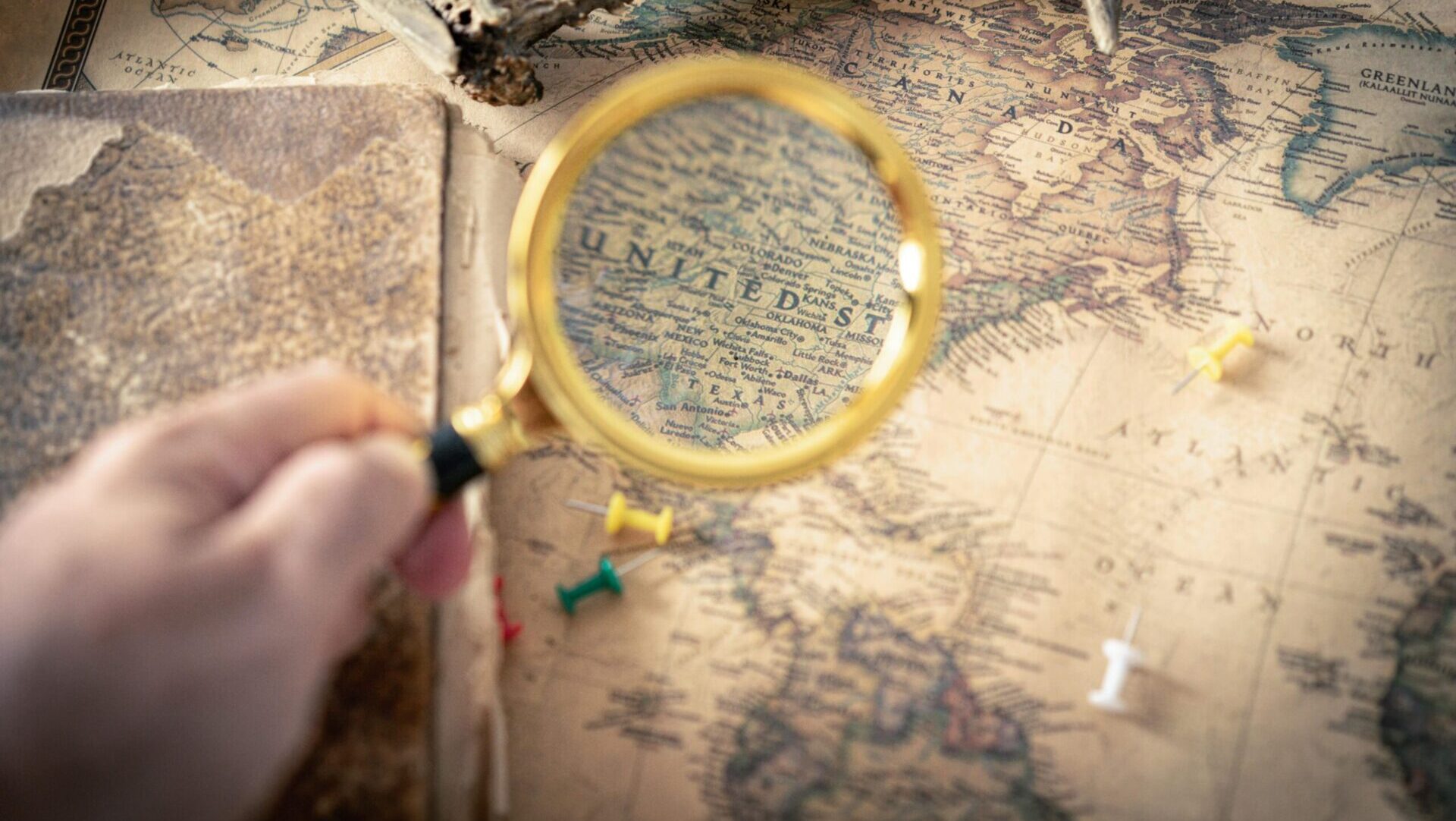 Hand holding a magnifying glass over a surface, symbolizing close inspection or search.