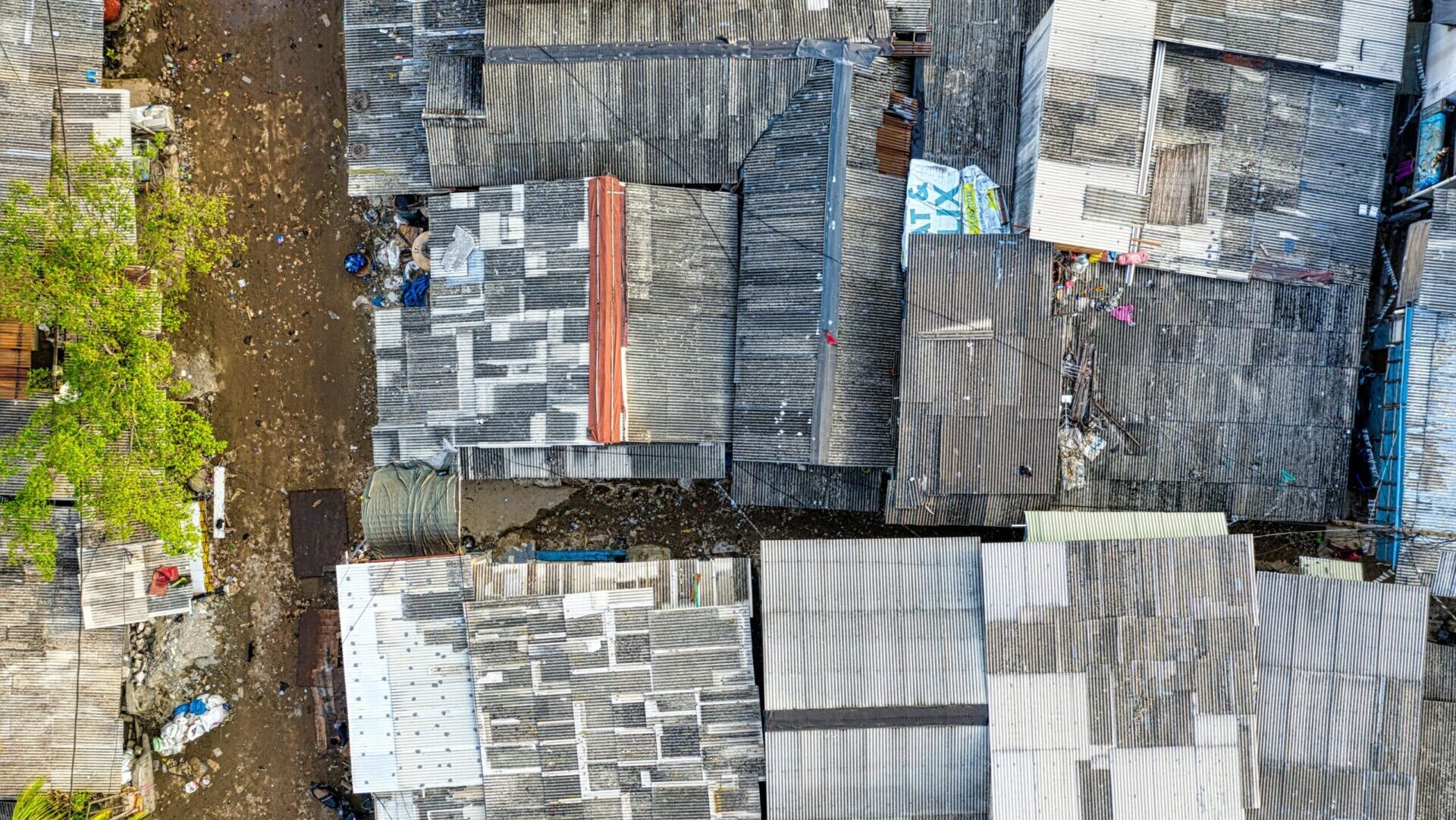 Close view of house rooftops near a dirt road in a crowded residential community.