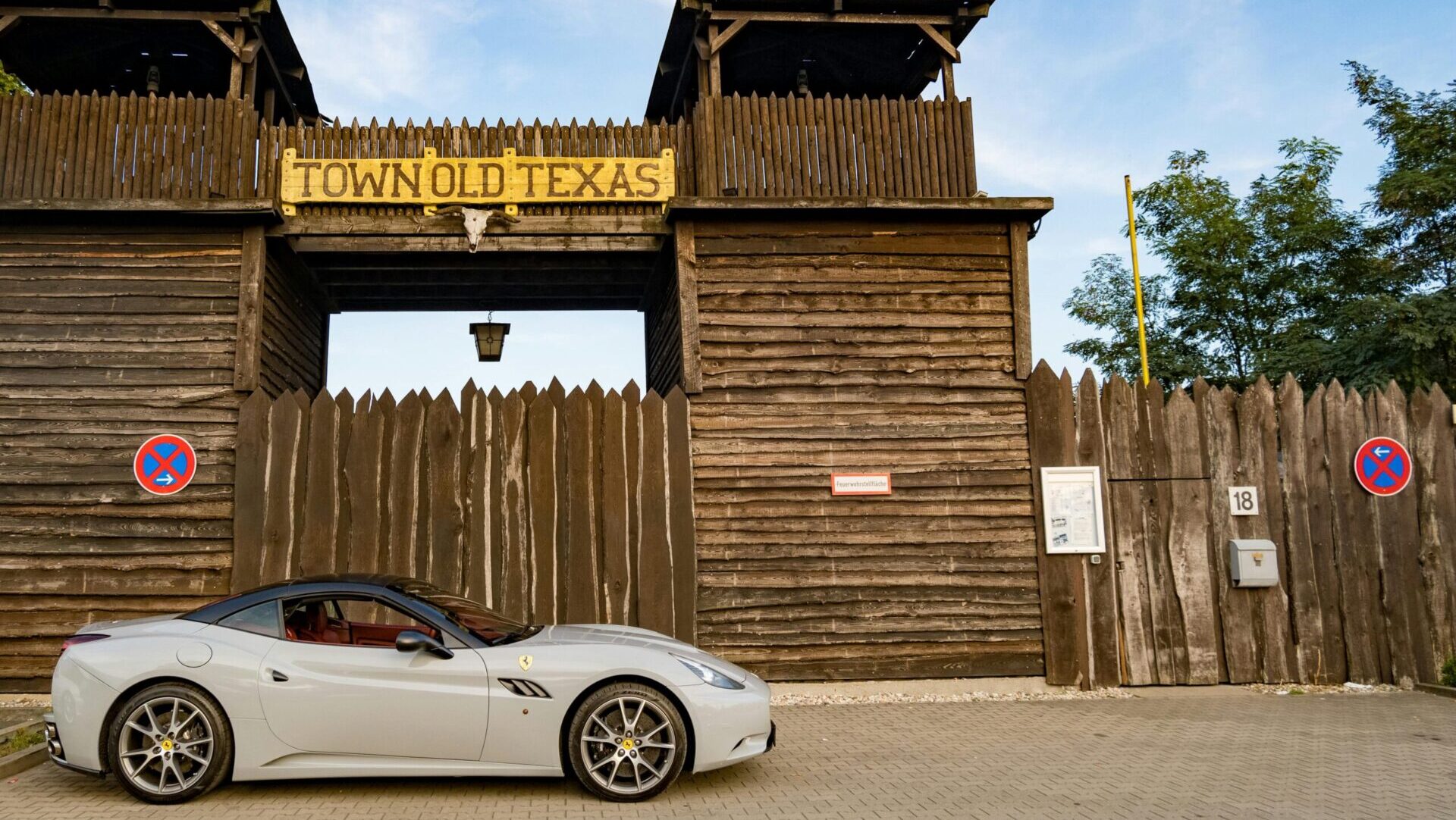 Red Ferrari California parked in front of an old Texas town gate, showcasing the car and rustic backdrop.