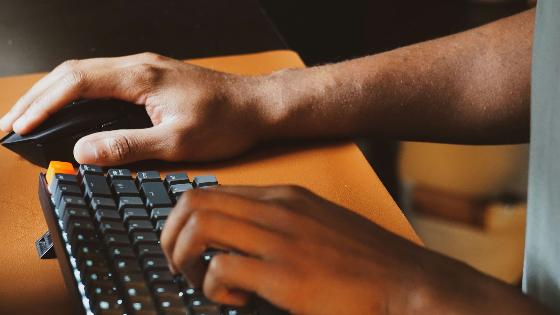 Person using a computer keyboard and mouse in an indoor workspace