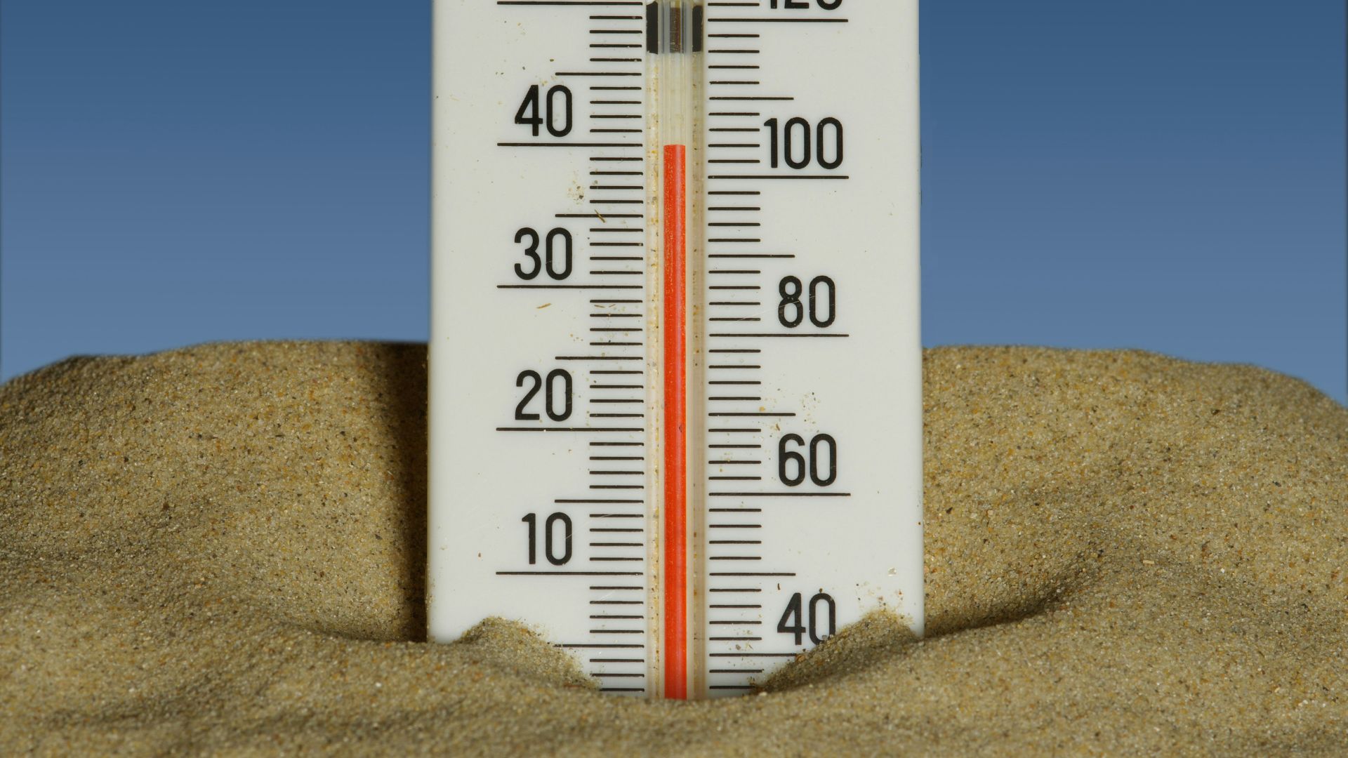 Thermometer placed in sand beneath a clear blue sky showing high temperature