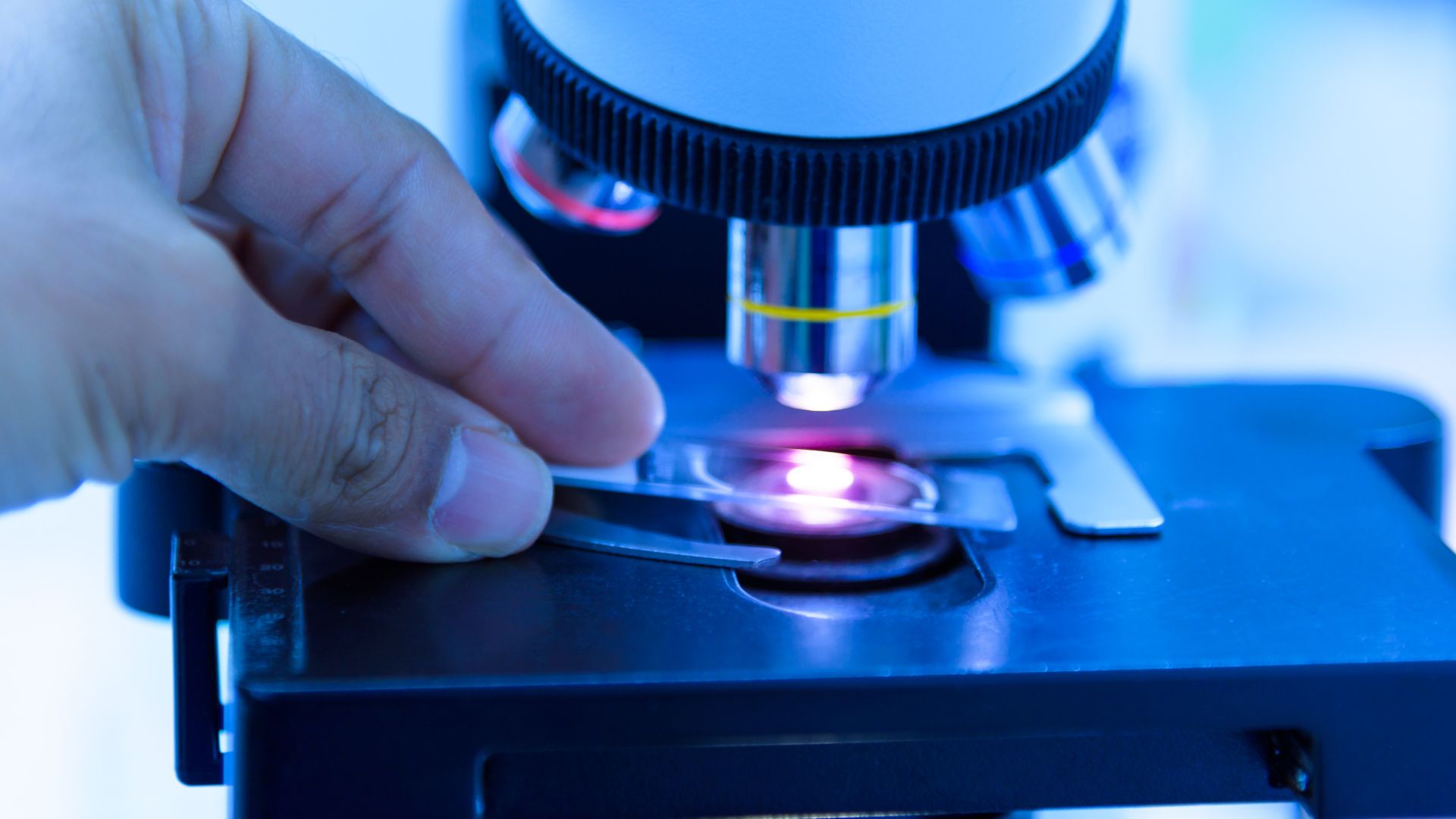 Close up of a hand putting a slide under a microscope