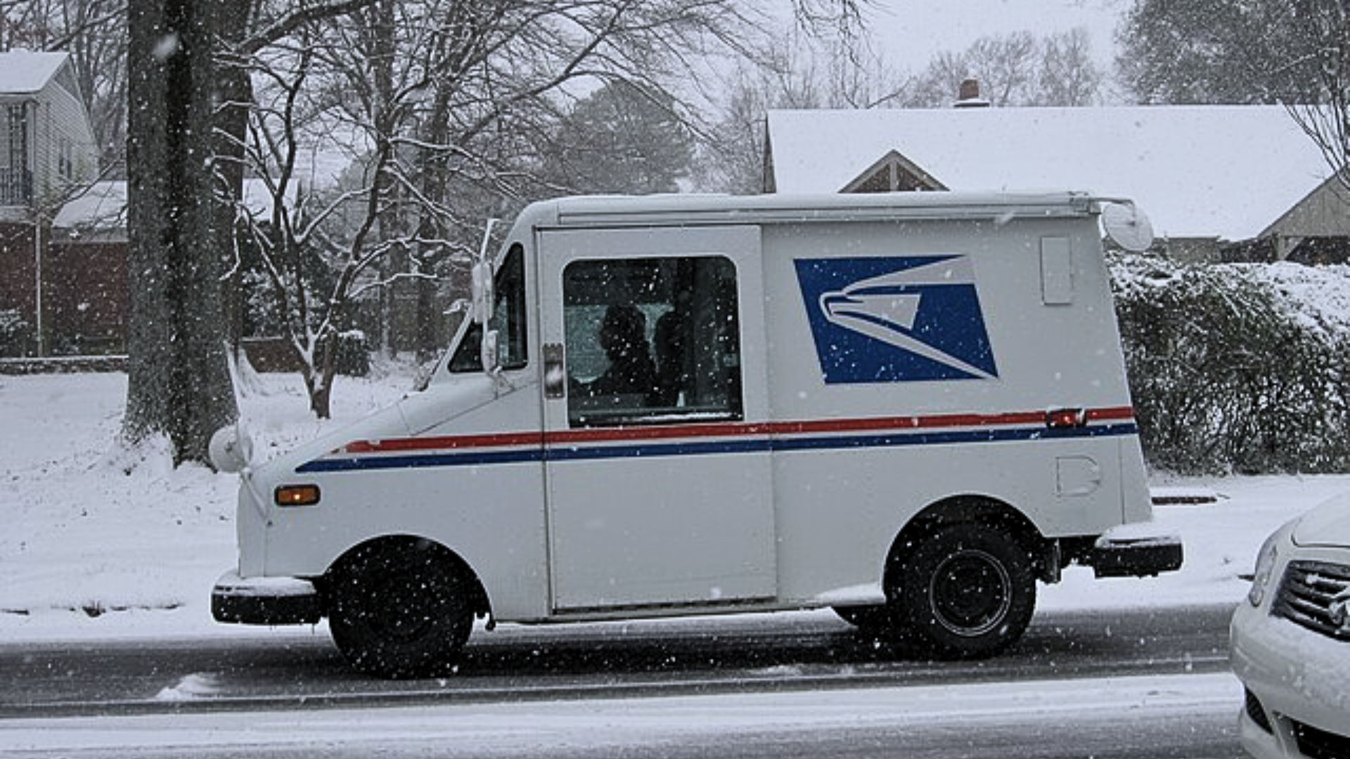 USPS mail truck driving through a snowy neighborhood.