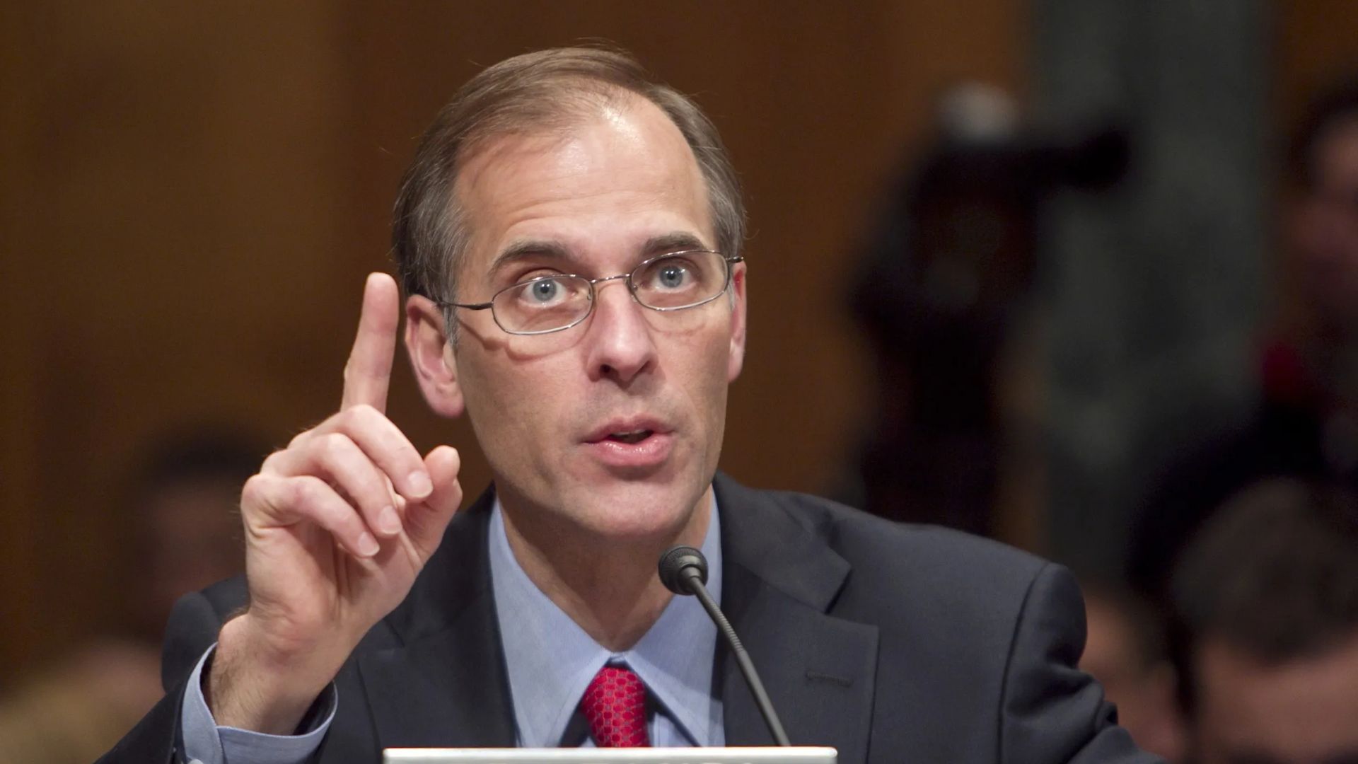 Mark Zandi speaking at a conference table while raising his index finger.