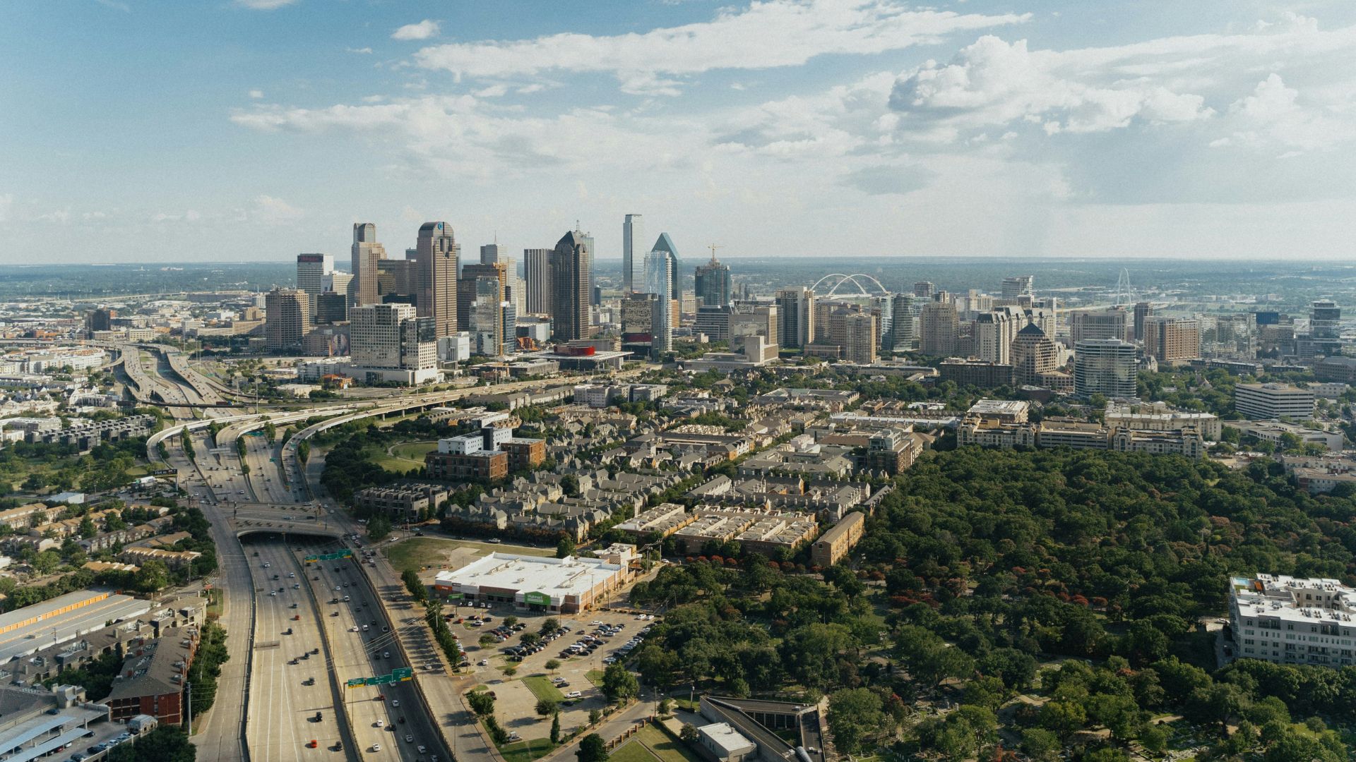 Aerial view of Dallas skyline with highways and surrounding neighborhoods in daylight.