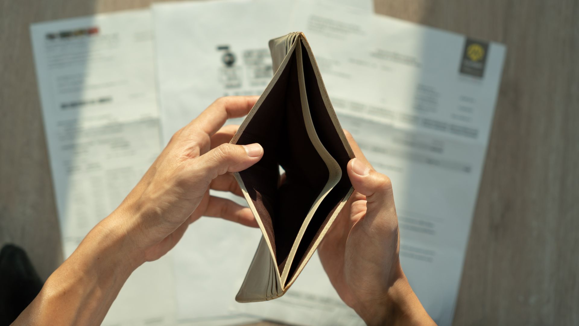 Man holding overdue bills and invoices while sitting at a table looking stressed.