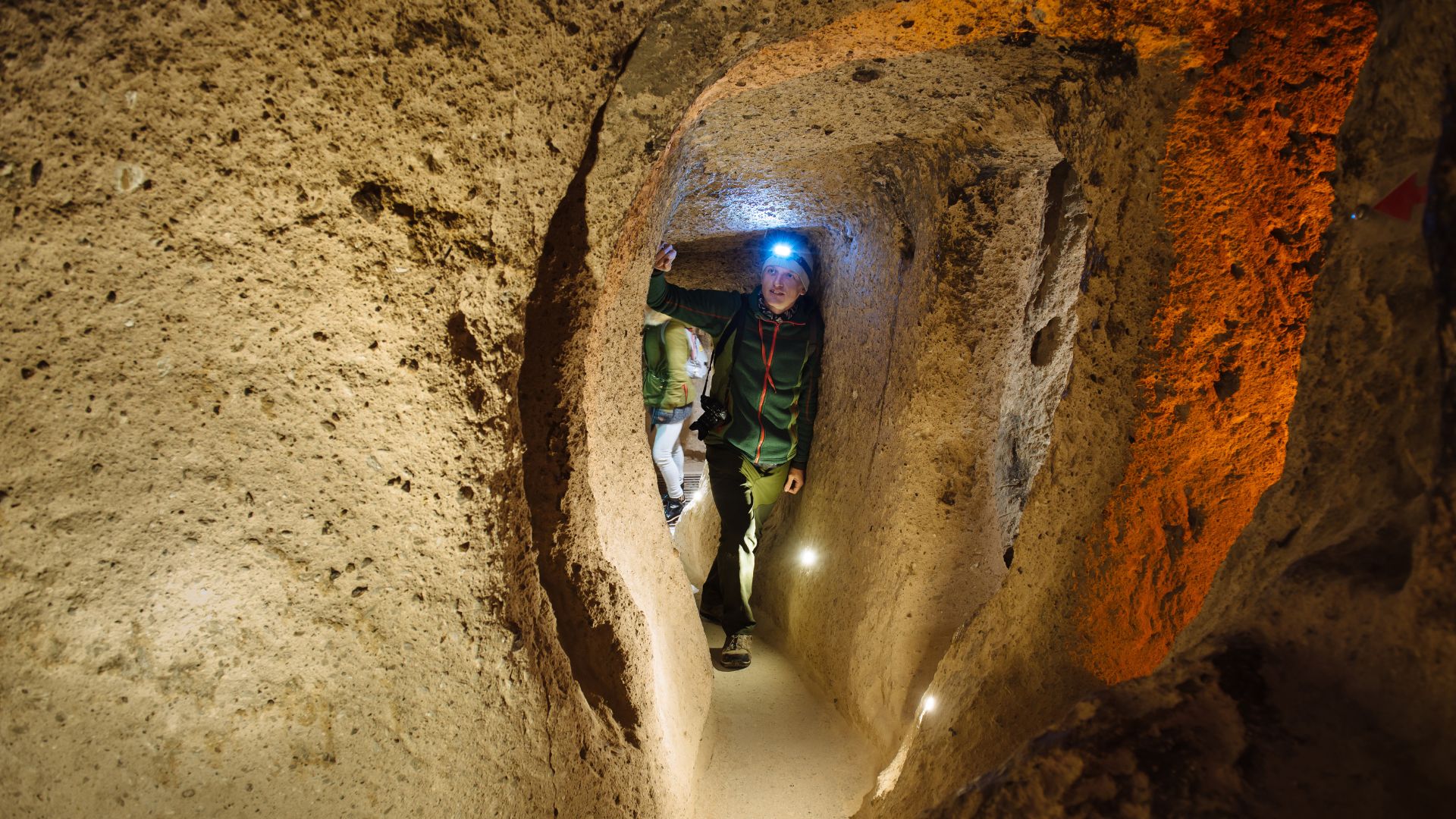 Tourists with headlamps examining cave walls inside an ancient underground chamber