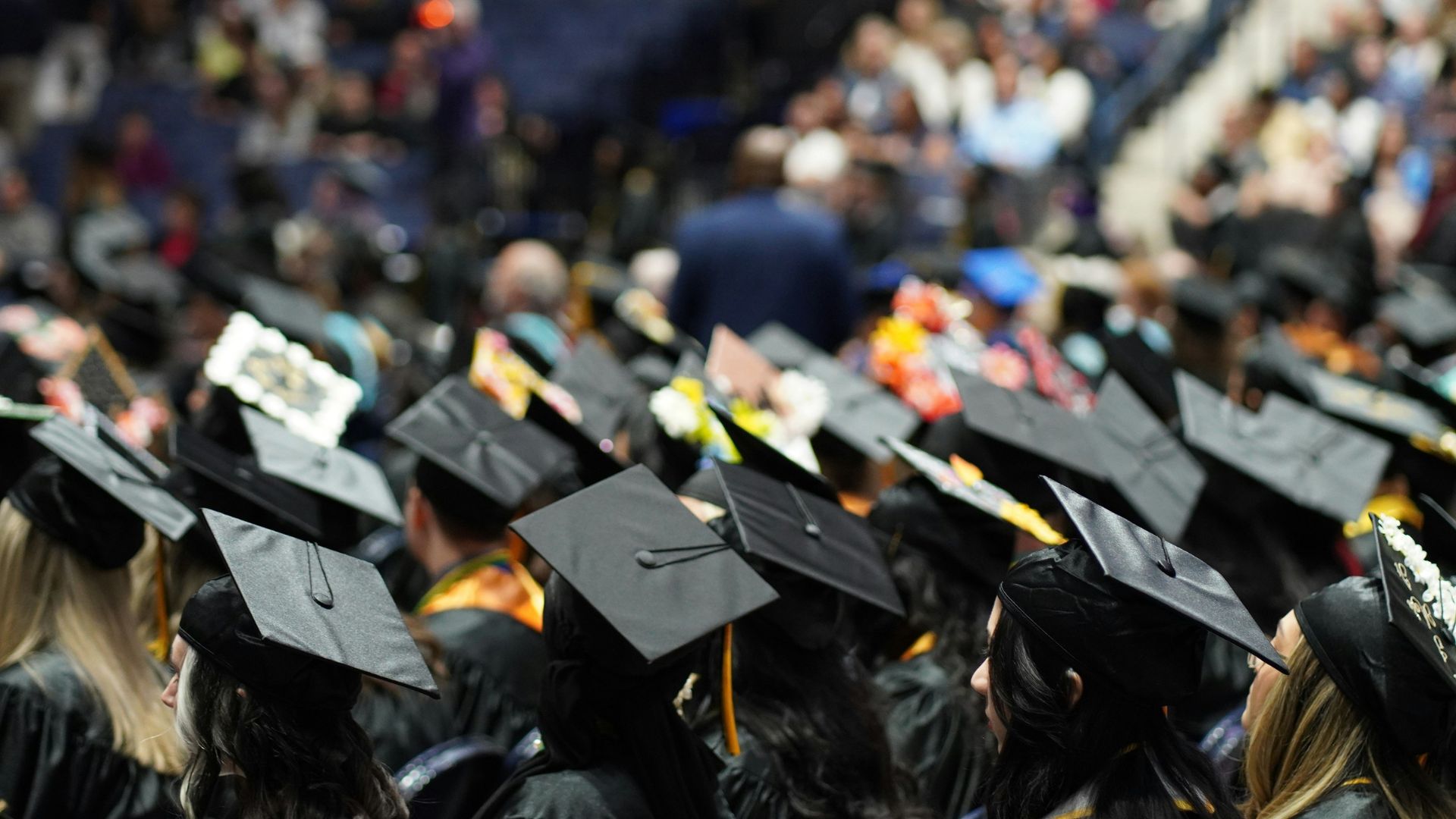 Graduates wearing caps and gowns seated during a university commencement ceremony.