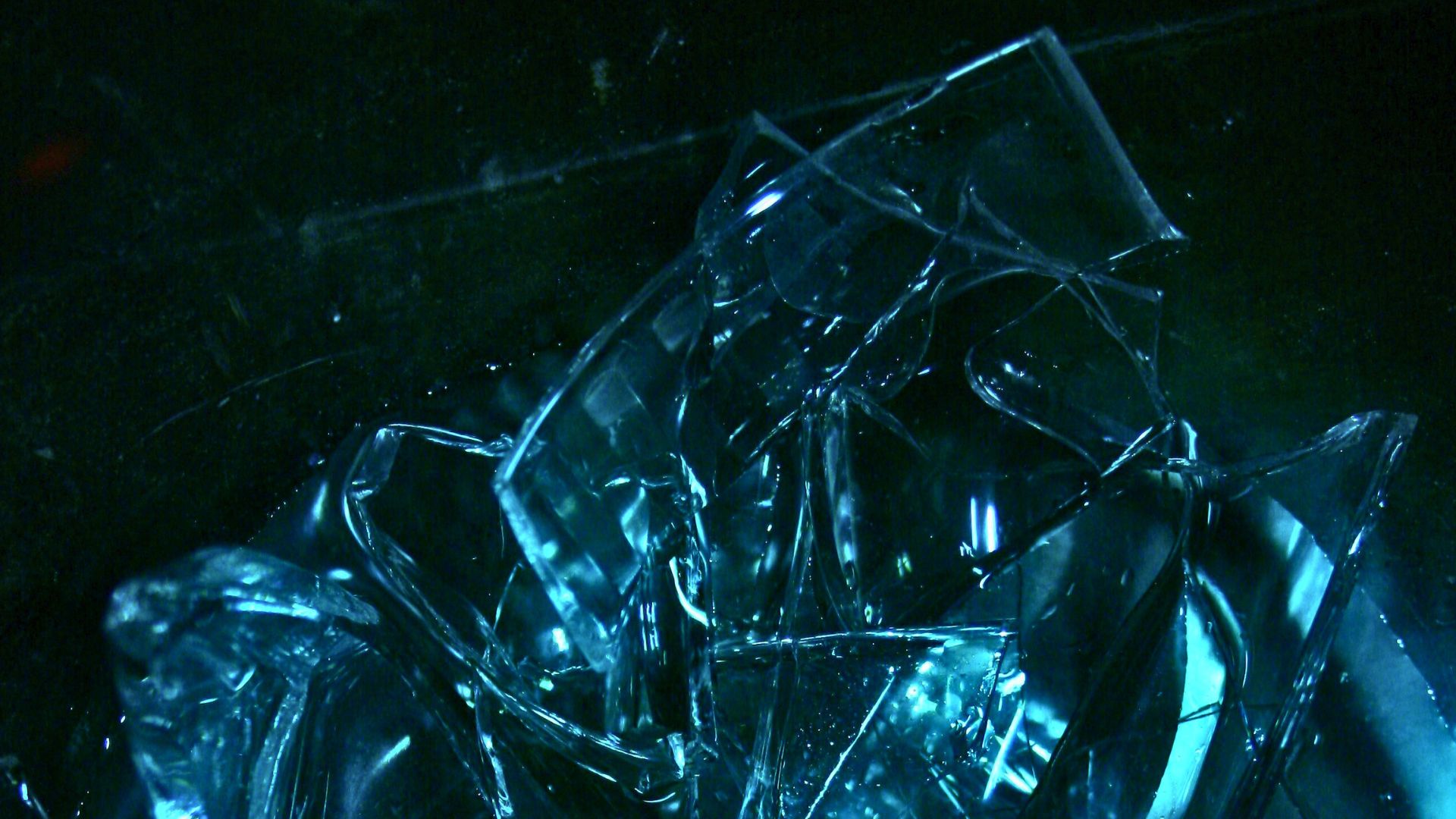 Close up of shattered glass pieces submerged in dark blue green water with light reflecting off the sharp edges.
