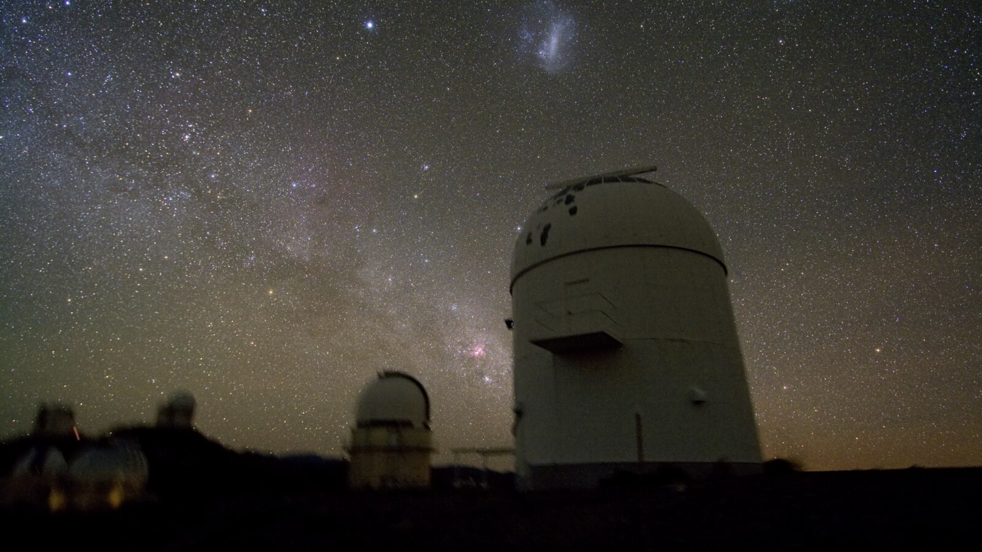 A nighttime view of an observatory with telescope domes beneath a star-filled sky.