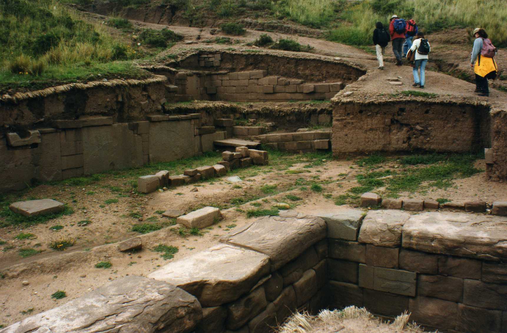 Visitors walking through the semi-subterranean temple at Tiwanaku, Bolivia, surrounded by carefully cut stone walls and foundations.