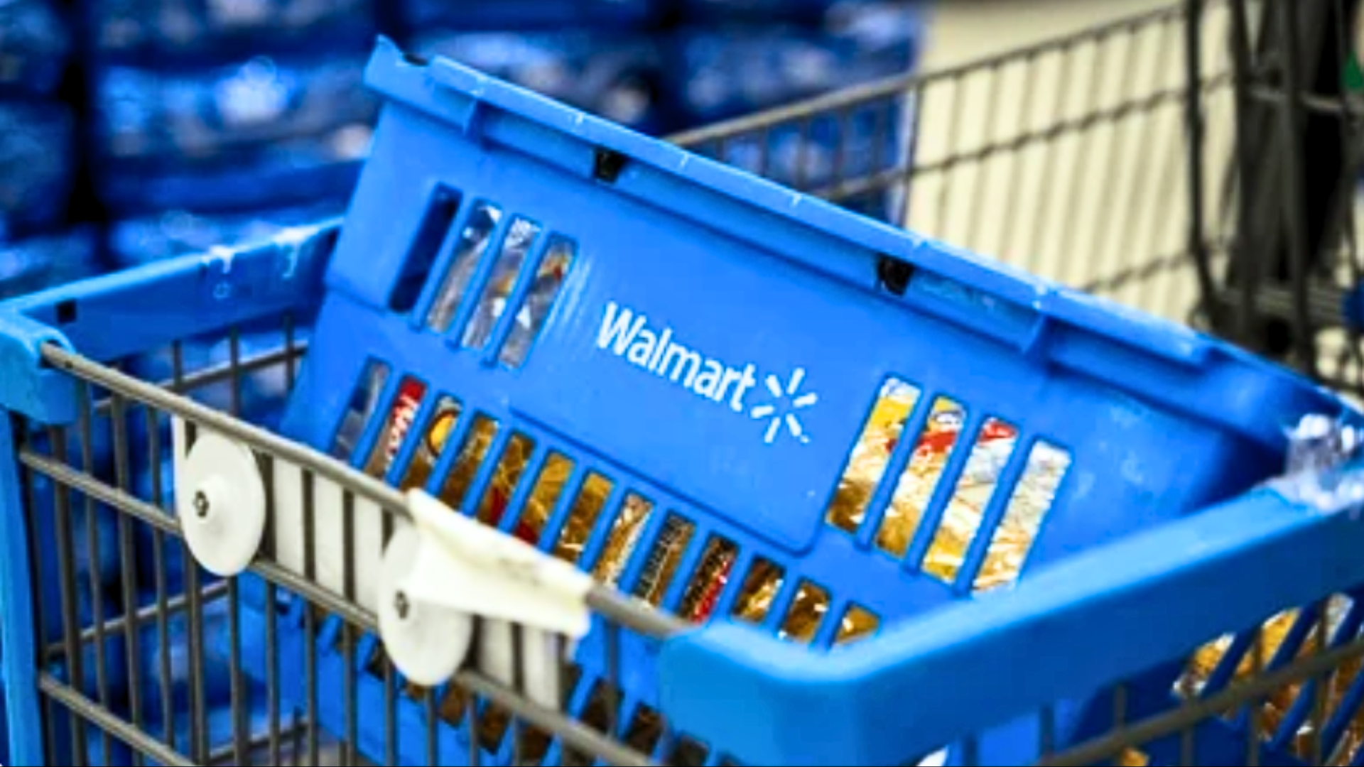 A close-up of a blue Walmart shopping basket filled with various grocery items resting inside a metal shopping cart.