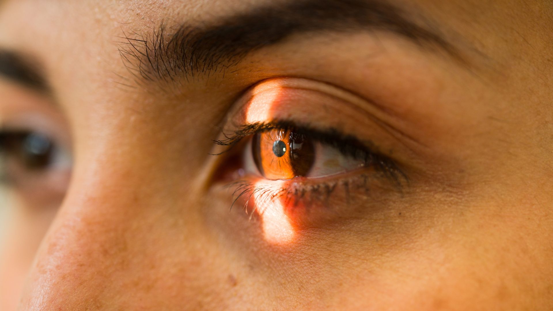 Close-up of a human eye illuminated by orange light highlighting the iris and pupil.