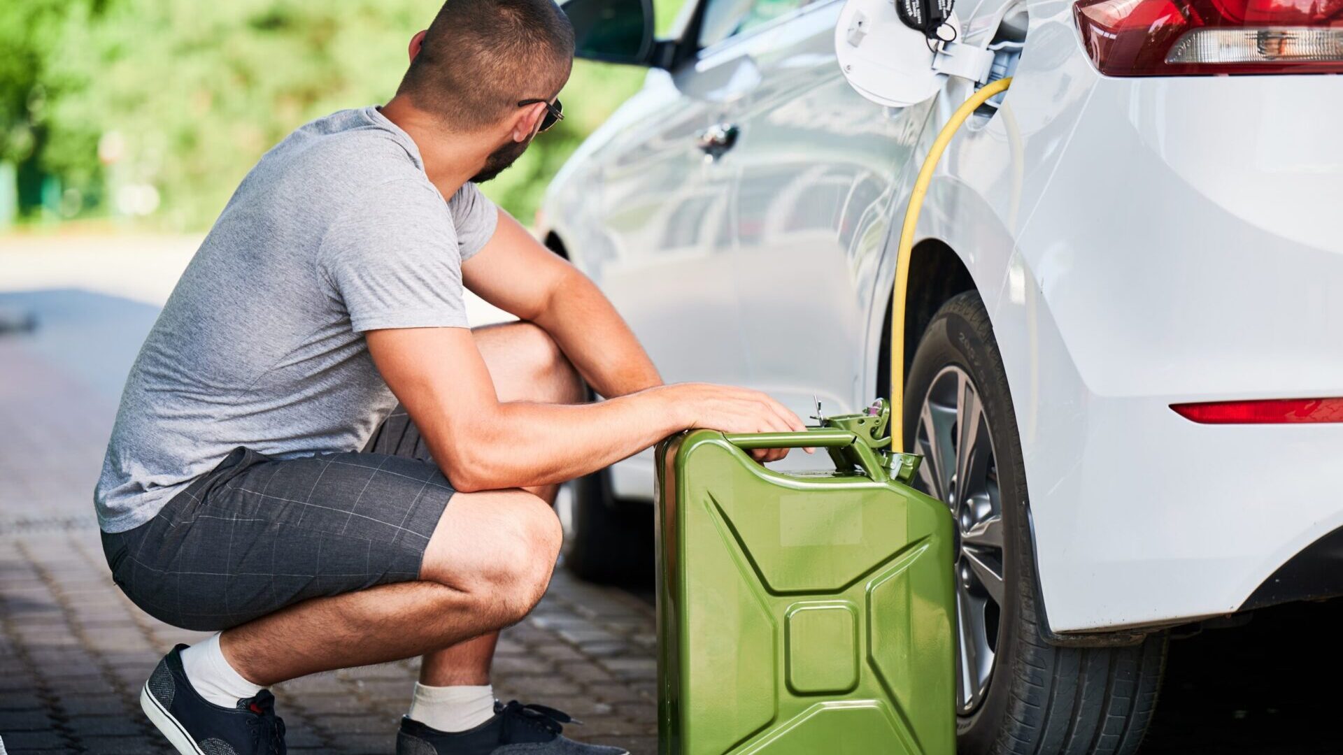 Man pouring fuel from a jerry can into a car parked outdoors.