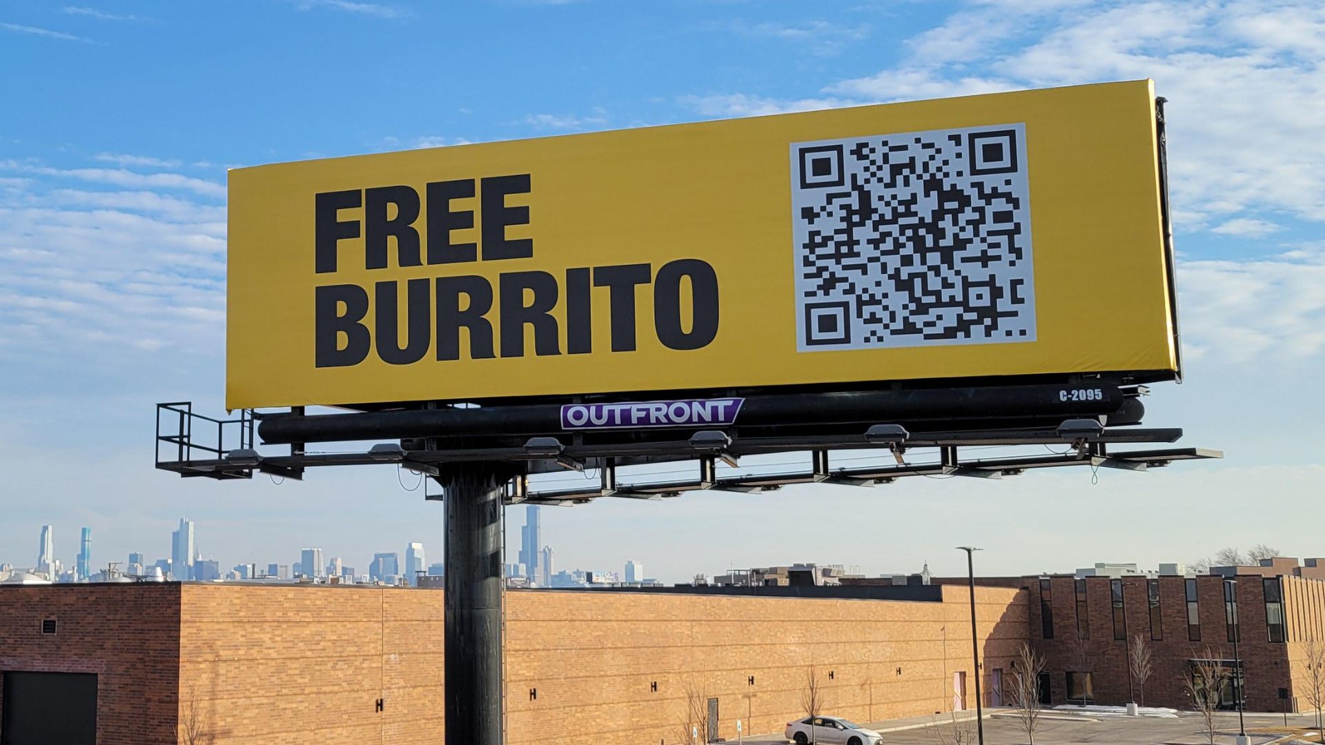 Yellow billboard advertising free burrito with QR code above city skyline.