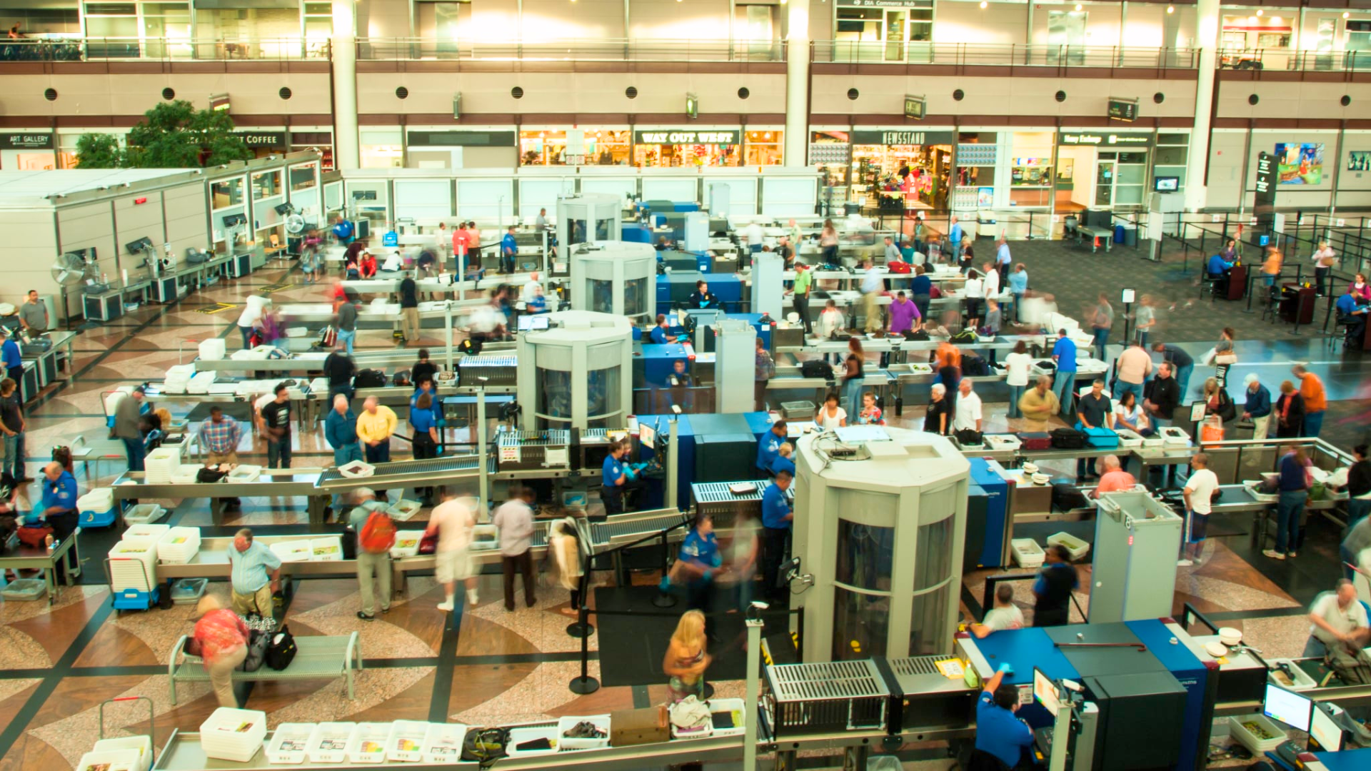 A high view shows a busy airport security area filled with people and machines.