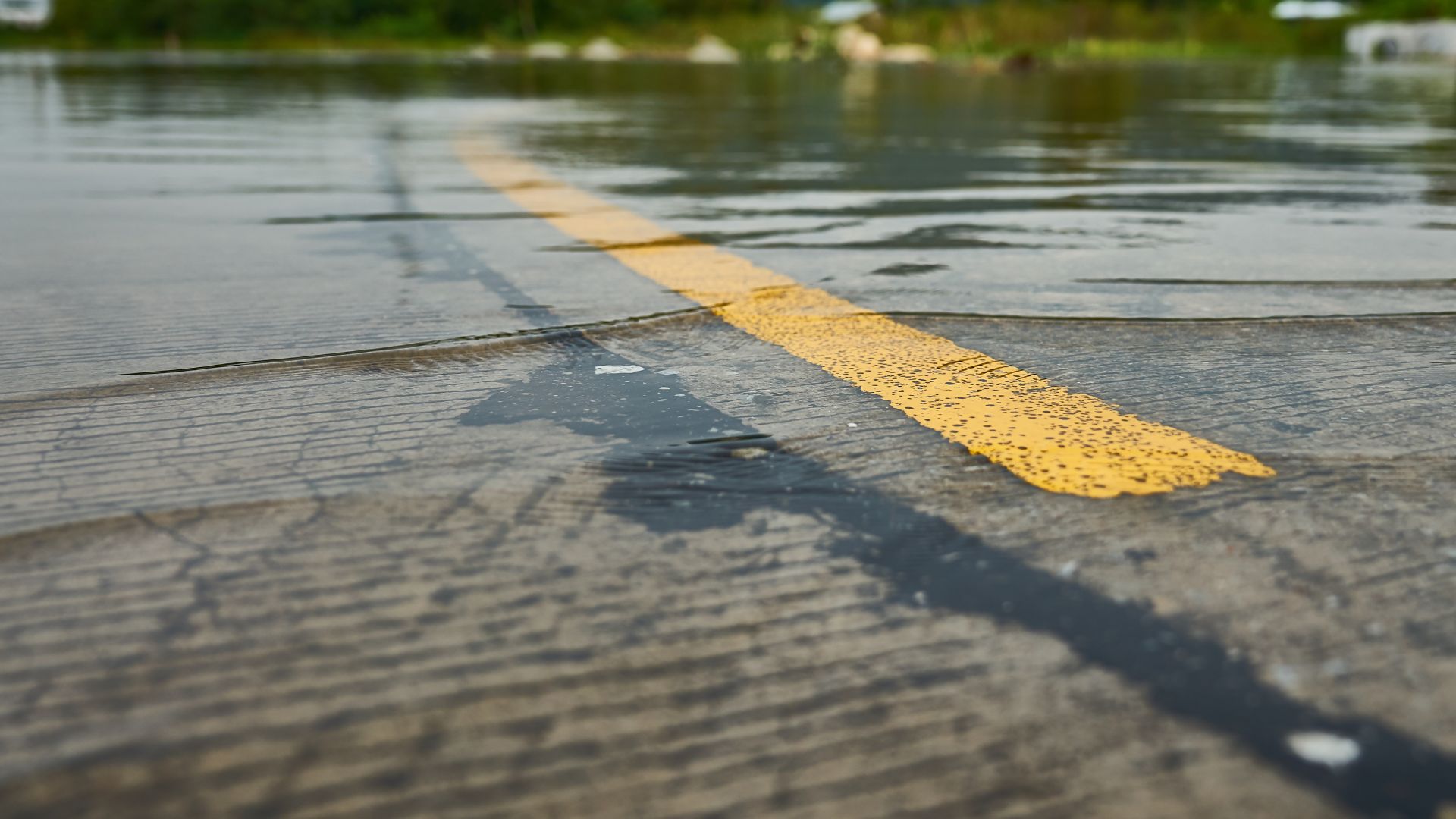 Floodwater covering road with yellow center line barely visible beneath shallow water.