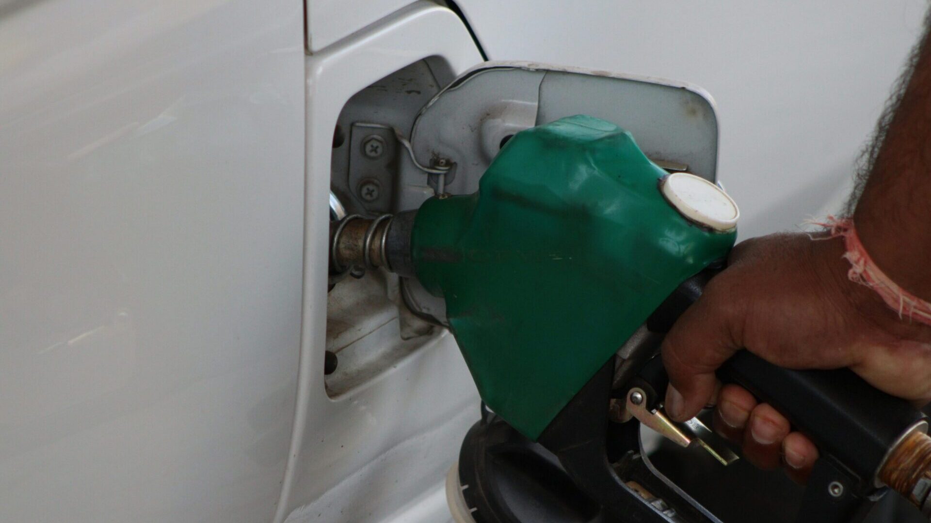 Hand holding a fuel nozzle while refueling a car at a gas station.