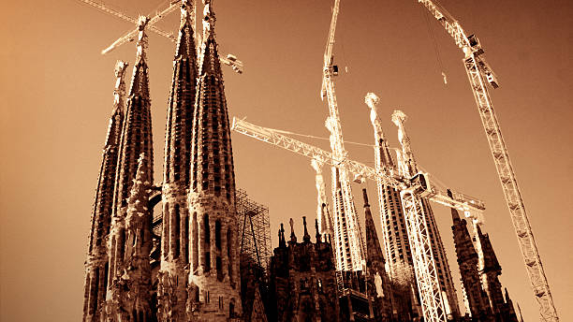 Sepia-toned view of the Sagrada Família cathedral under construction with multiple large cranes in Barcelona.