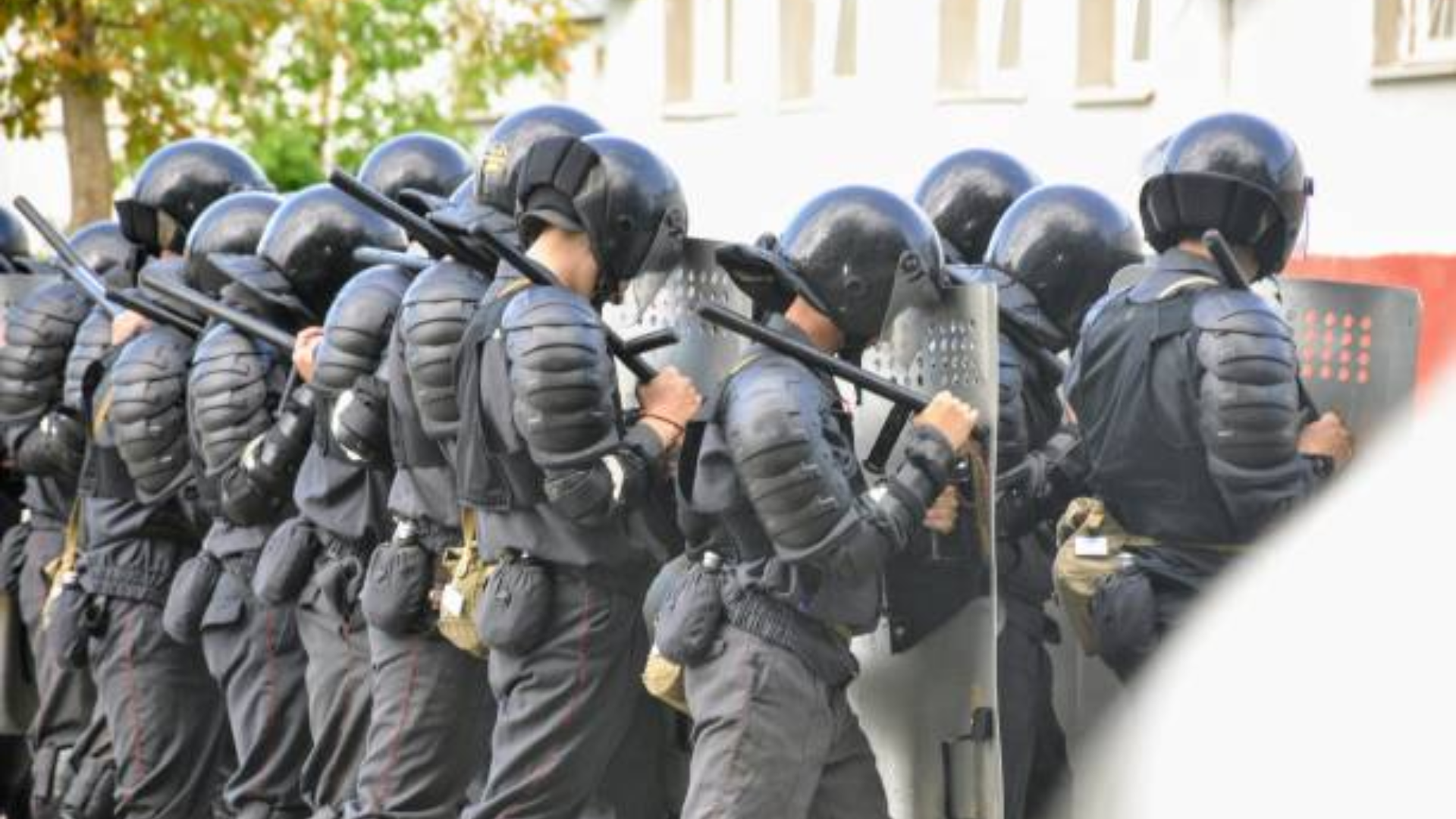 Line of police officers in riot gear holding shields and batons.