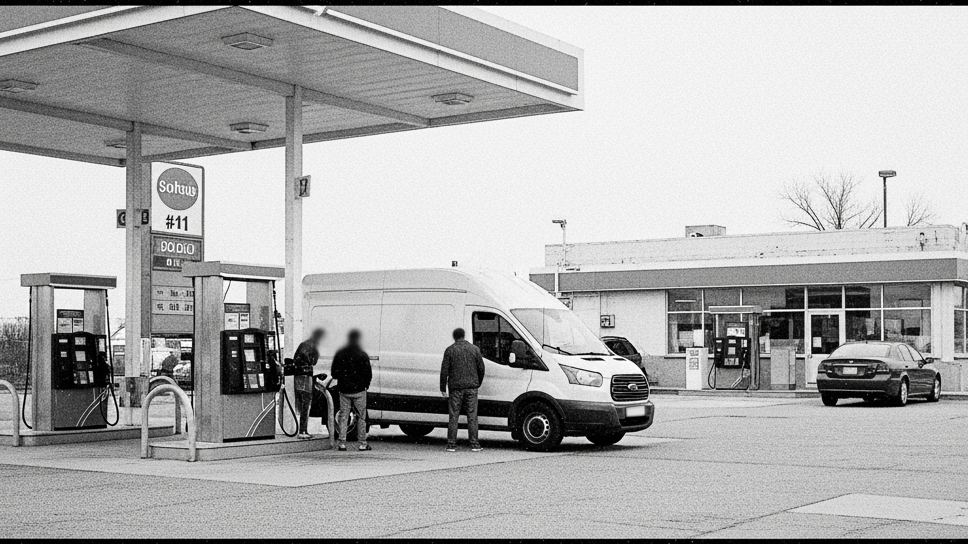 A greyscale picture of a gasoline station with people getting gas.