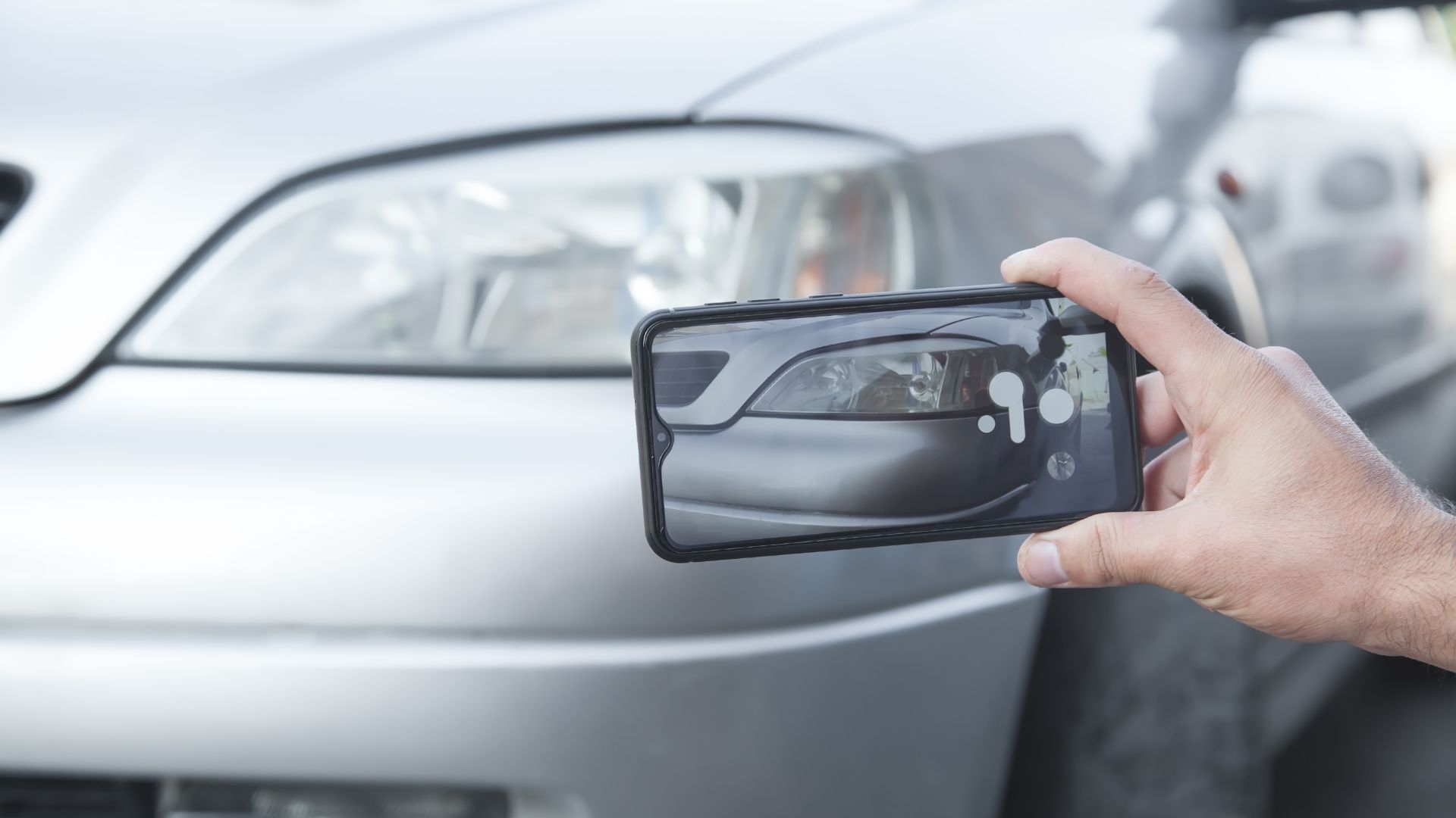 Person holding a smartphone close to a car headlight while photographing the vehicle.