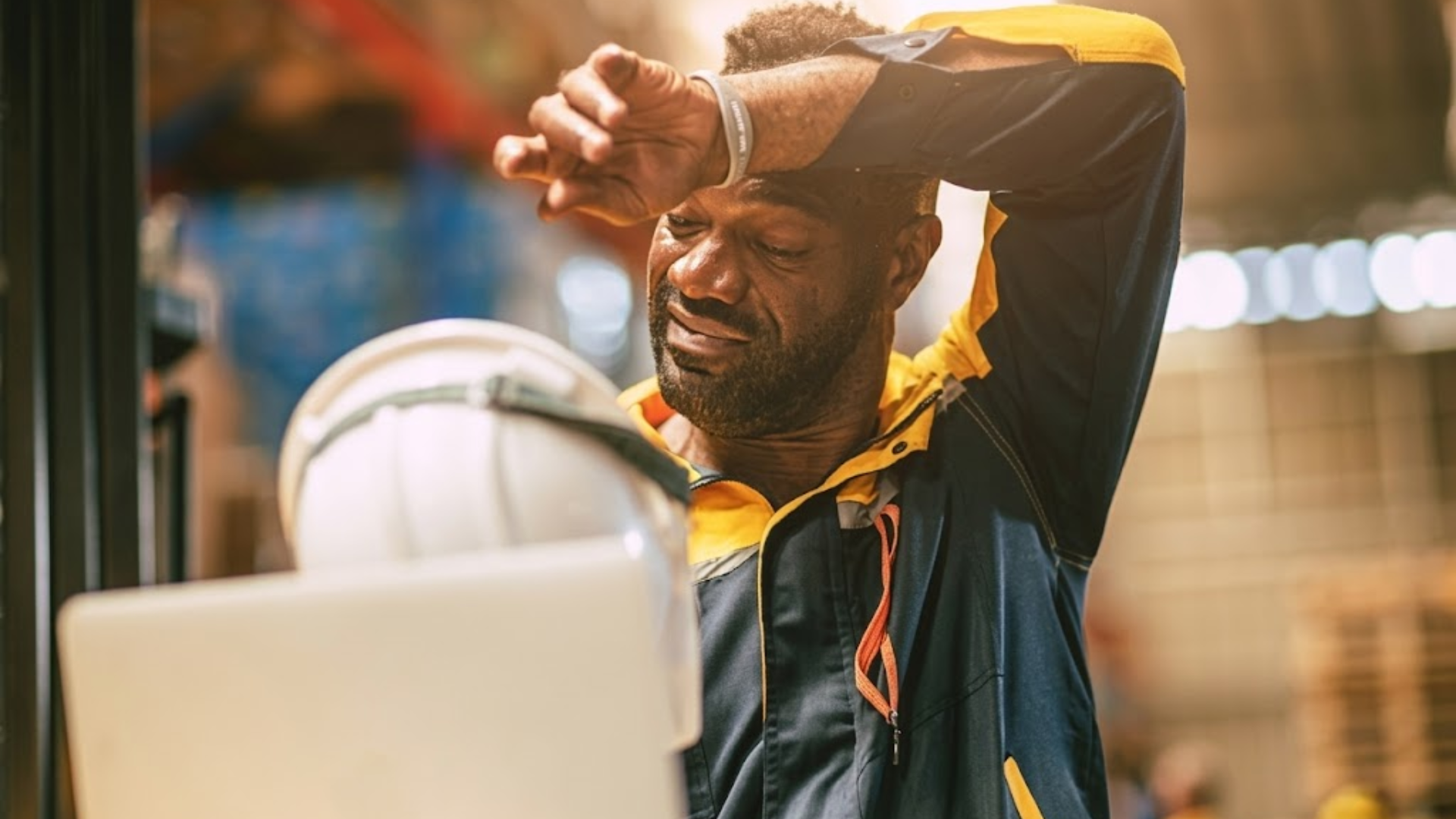 Man wiping sweat from his forehead while standing outdoors in warm conditions.