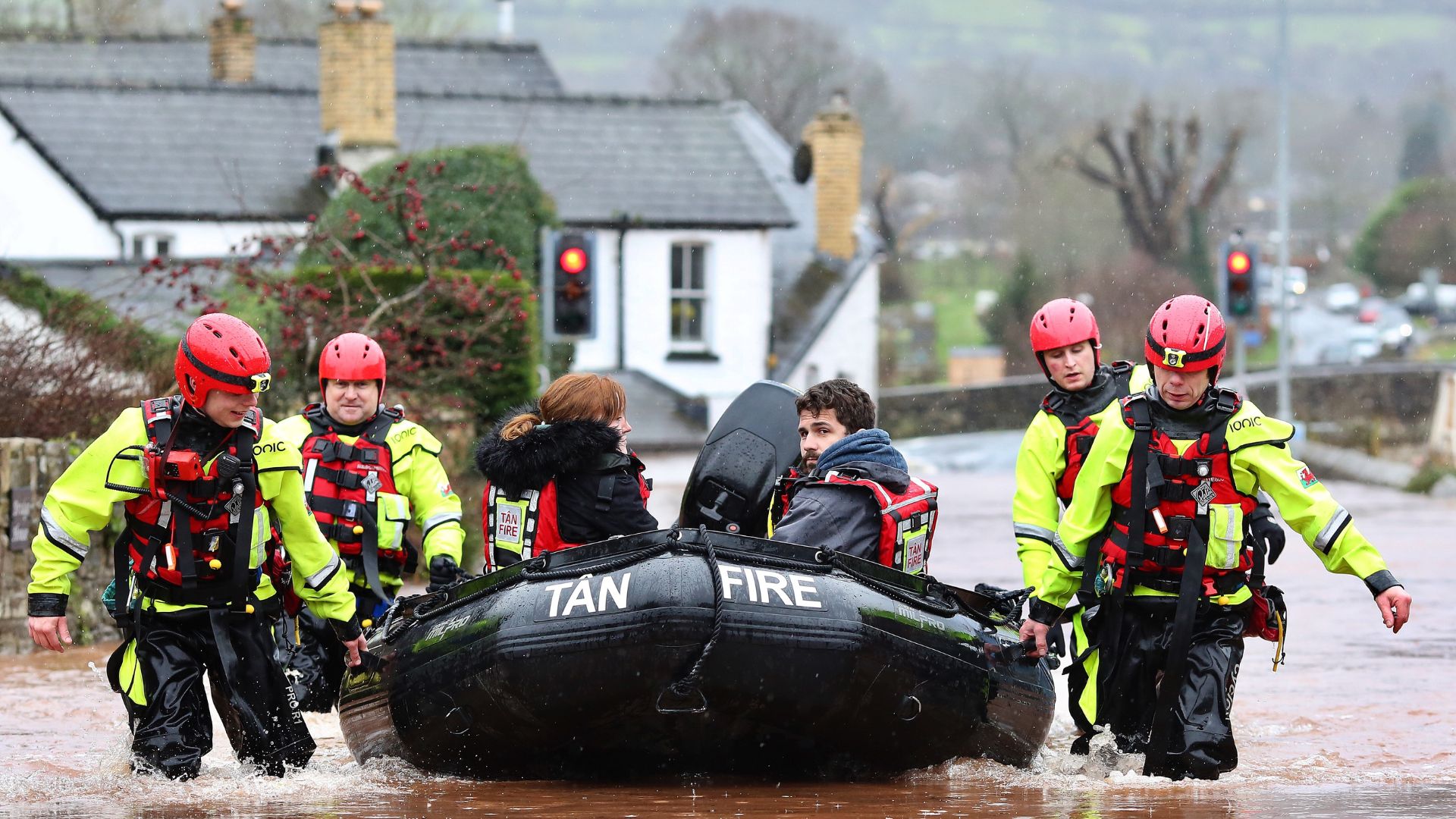 Rescue crews carrying inflatable boat through floodwater while evacuating residents in storm-hit town.