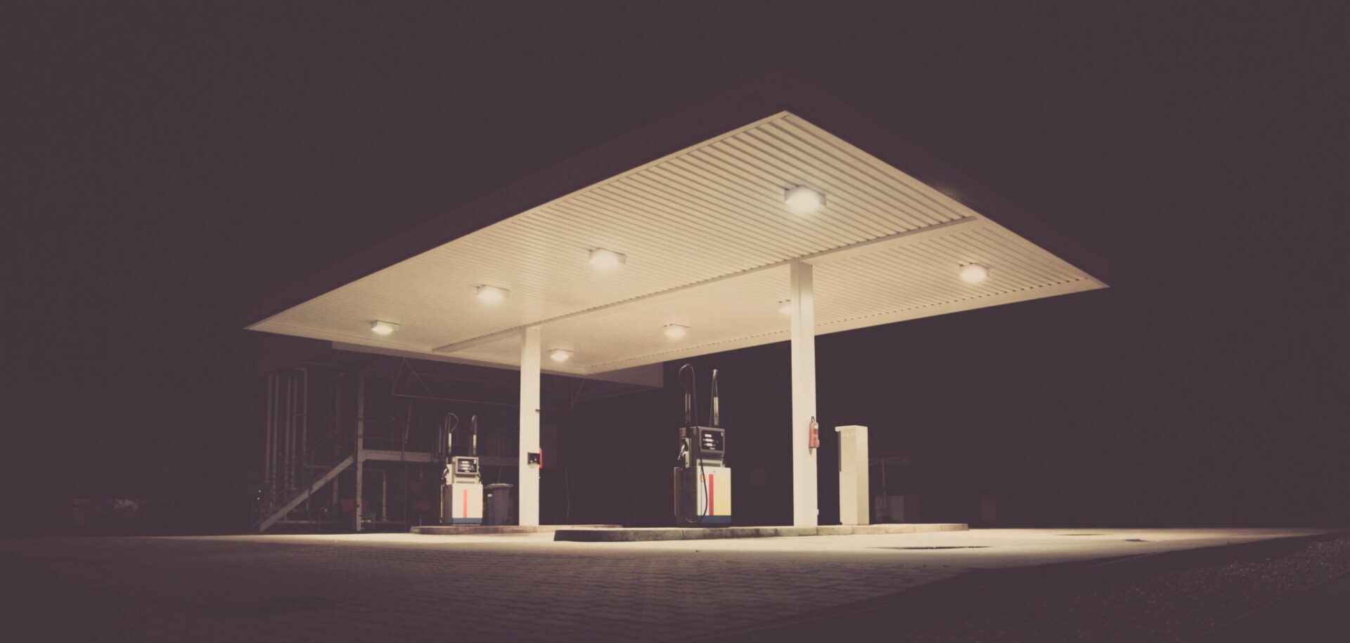 Empty gas station with bright canopy lighting and fuel pumps at night.