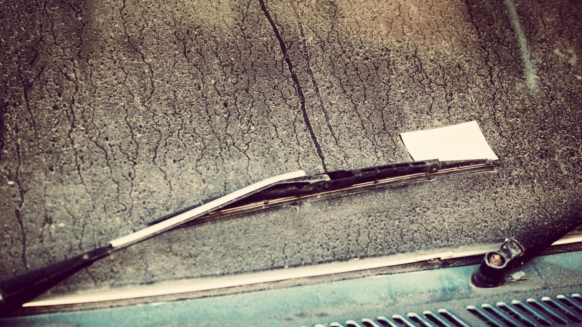 Windshield wiper on a dusty car windshield with streaks and dirt marks.