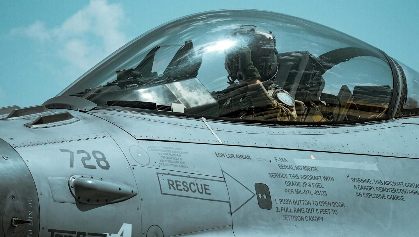 Fighter jet cockpit with pilot visible through the canopy during flight.