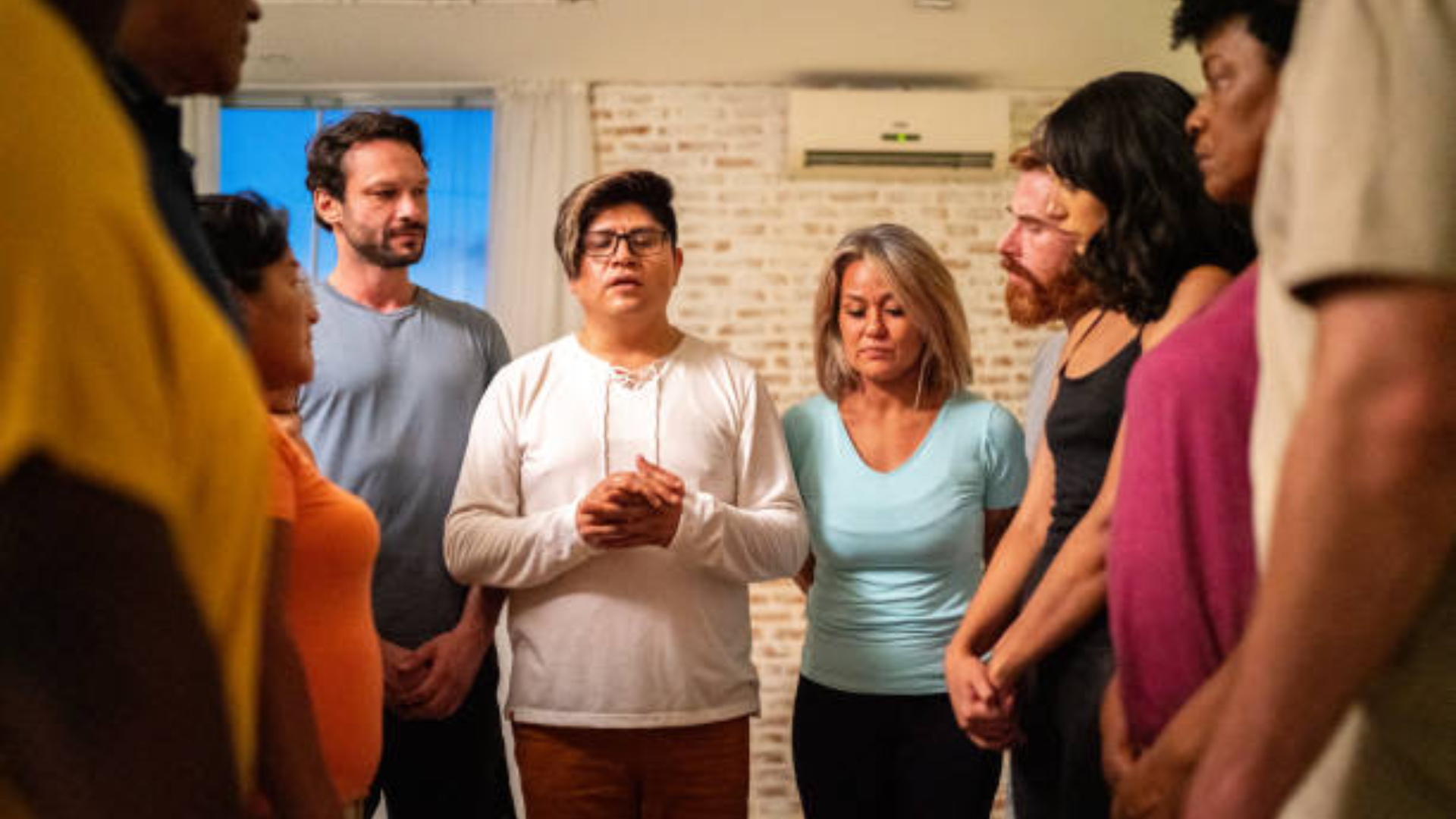 Group of people standing in a circle with heads bowed in prayer.