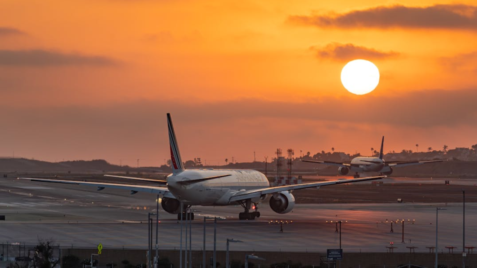 Two large airplanes rest on the runway under a beautiful orange sunset.