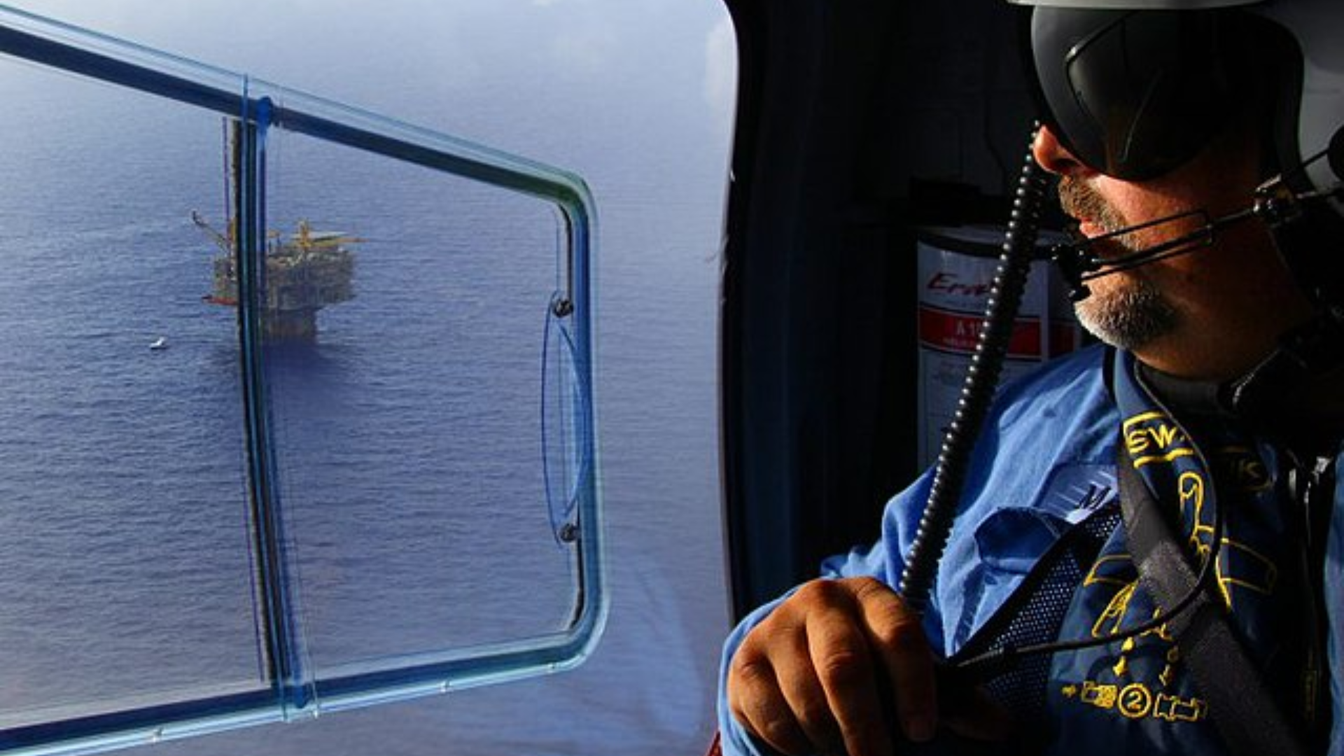 Aerial view from a helicopter window looking down at an offshore oil platform.