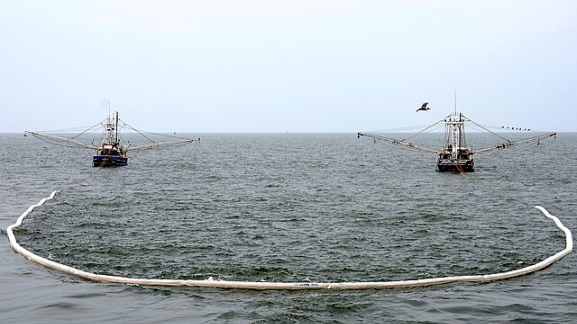 Two specialized boats deploying long, floating white containment booms.