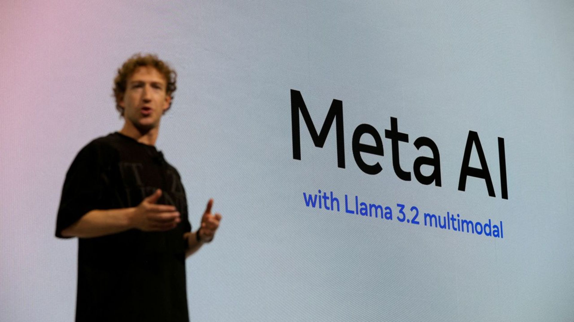 Mark Zuckerberg speaking at an event, with a large screen behind him displaying Meta AI.