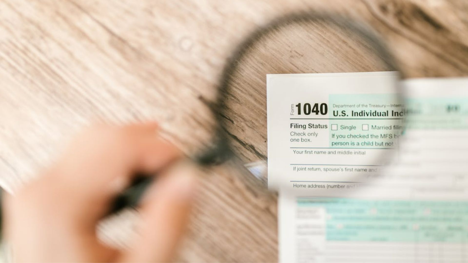 Magnifying glass held over IRS Form 1040 individual income tax return on wooden surface.