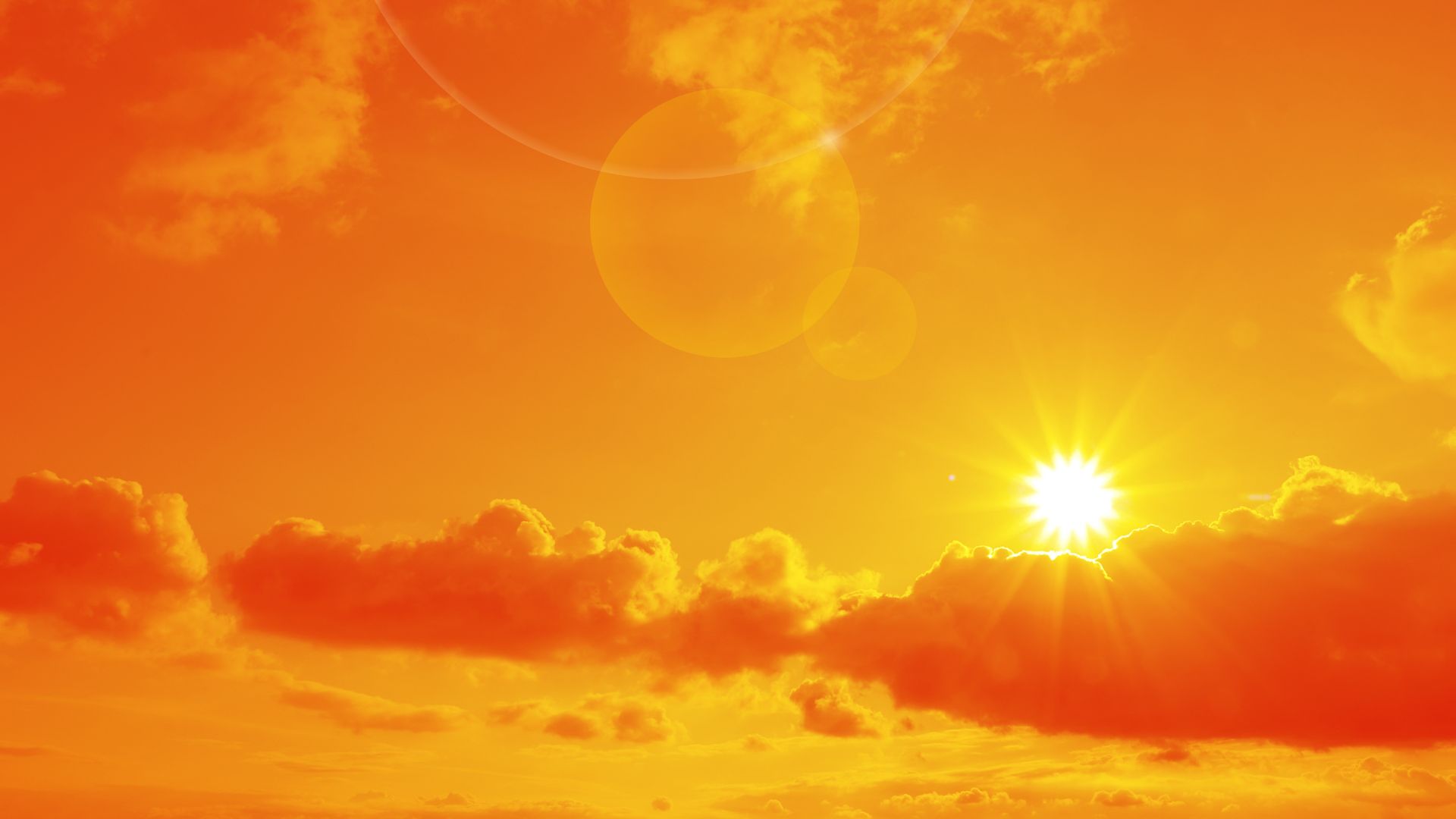 Orange sky with sun and clouds during hot summer weather.