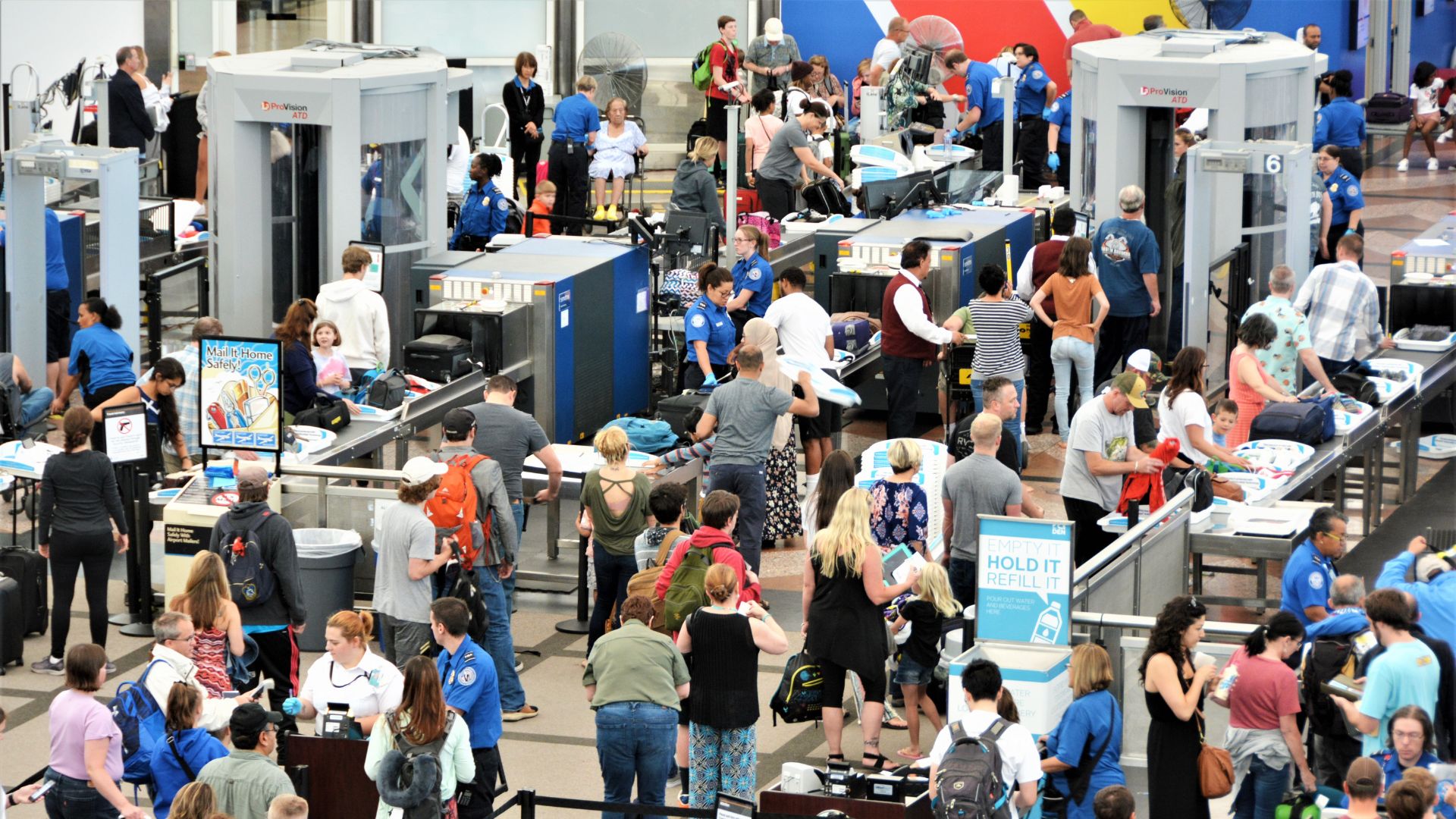Travelers in long lines at an airport going through security screening areas to get to their flights.