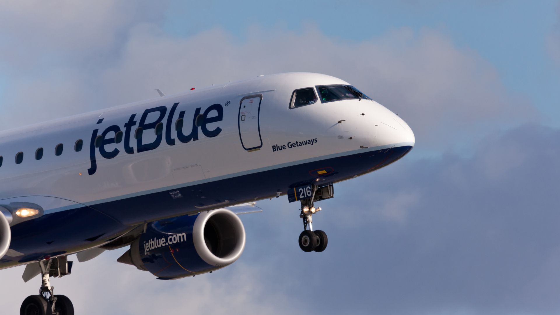 JetBlue airplane in flight against a backdrop of blue sky with clouds.