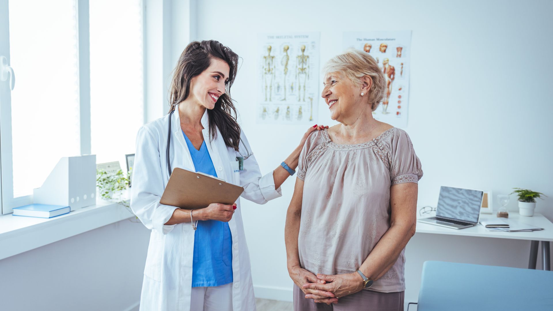 A doctor with clipboard smiling with elderly patient in bright medical office.