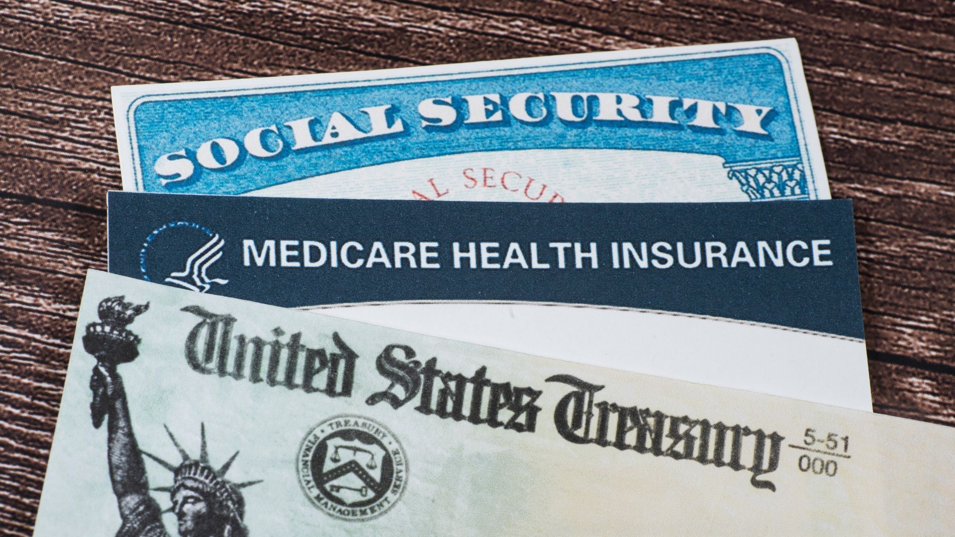 Social Security card Medicare health insurance card and US Treasury check on wooden surface.