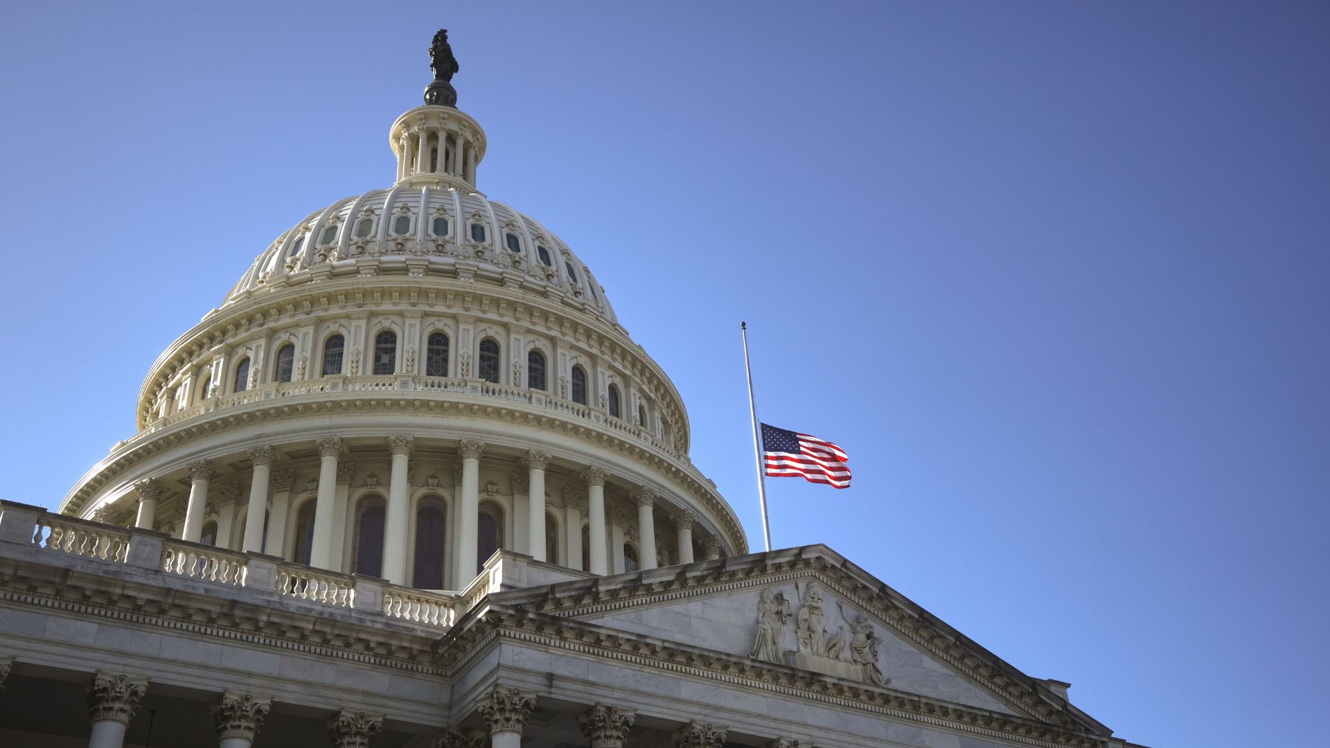 The Capitol Hill in Washington, DC with a flag waving in the wind under a blue sky.