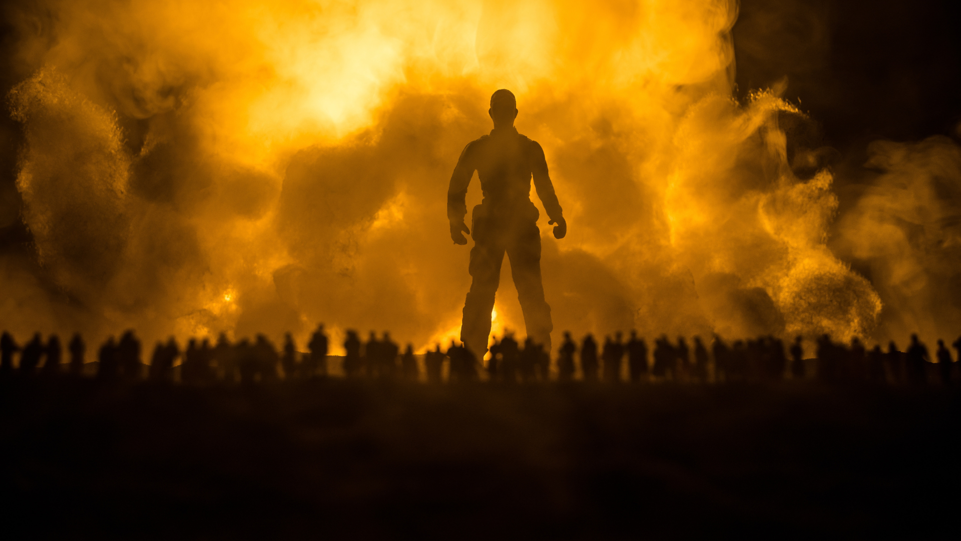 The silhouette of a Giant standing before a massive, fiery orange explosion with a crowd of people in the foreground.