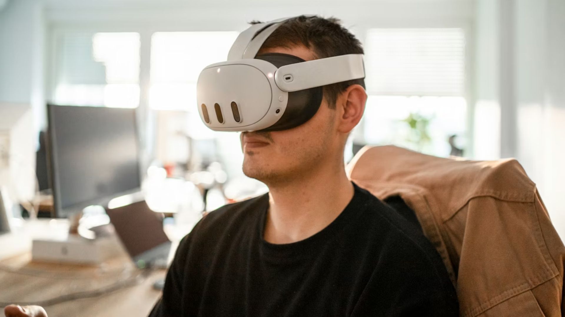 A man sitting at an office with a Meta Quest headset over his eyes.